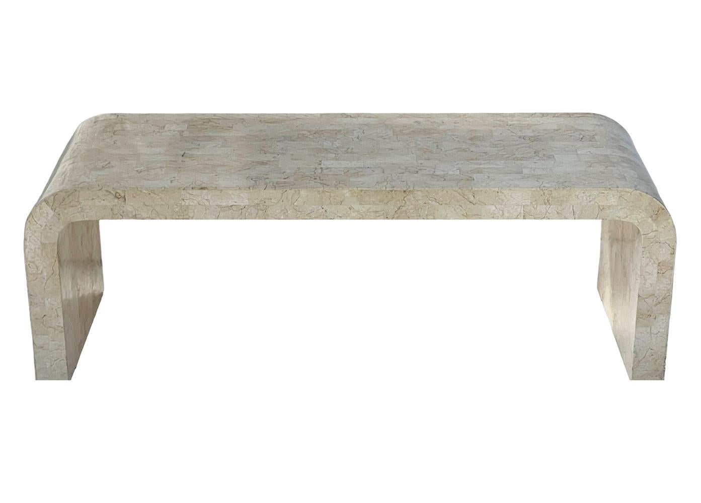 A classic waterfall form coffee table straight out of the 1980's. It features a tessellated stone finish in a cream colored marble. 