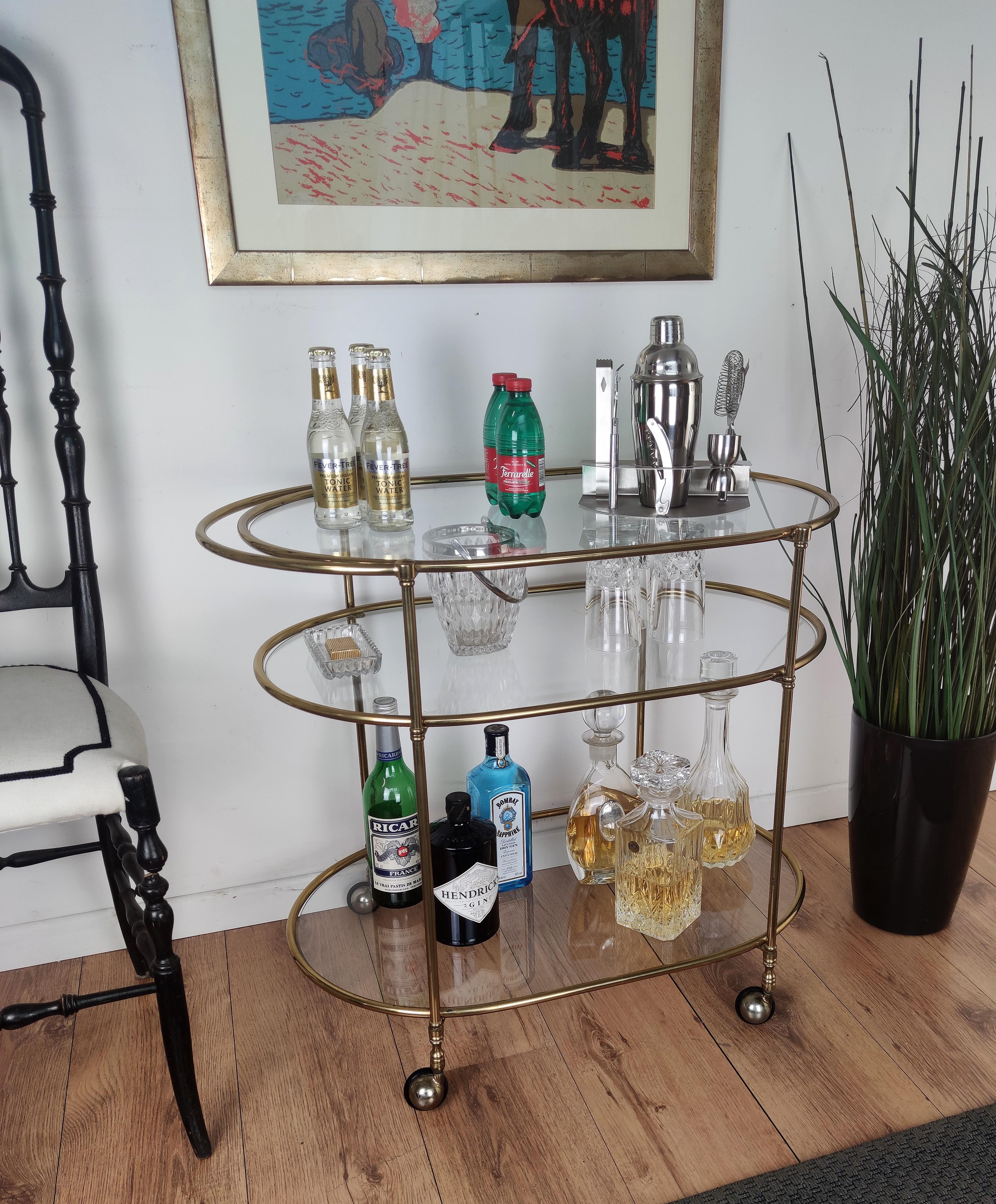 Beautiful and stylish vintage 1970s Italian three-tier brass and glass bar cart oval shaped in very good conditions. A great piece that perfectly adds to every home decor the typical glitz, glamour and gold of Hollywood Regency style, with a nod to