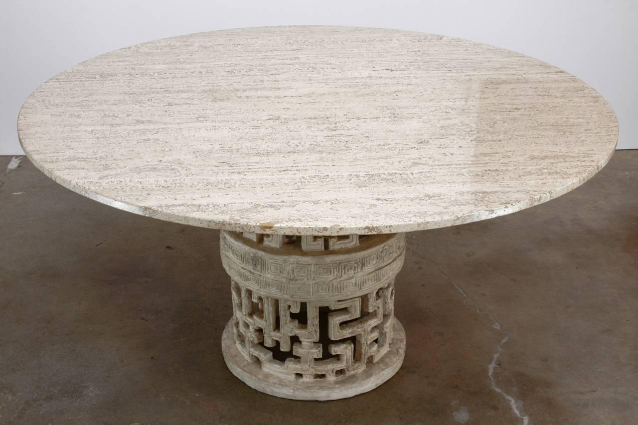 Stunning Hollywood Regency travertine dining table with a molded stone pedestal base. The interesting base features an open fretwork of geometric Greek key designs in a round shape. The round top of solid travertine has a smooth polished finish.