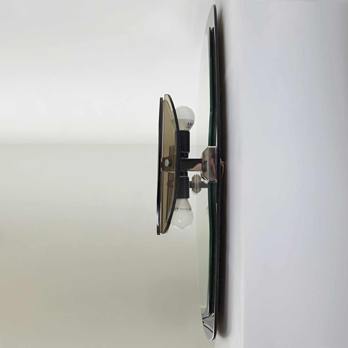Ce miroir de grande classe a été fabriqué par Veca, vers les années 1960.
Le miroir a une forme ovale et un cadre de miroir de couleur laiton. Sur les côtés gauche et droit, le miroir contient quatre ampoules derrière une combinaison de verre clair
