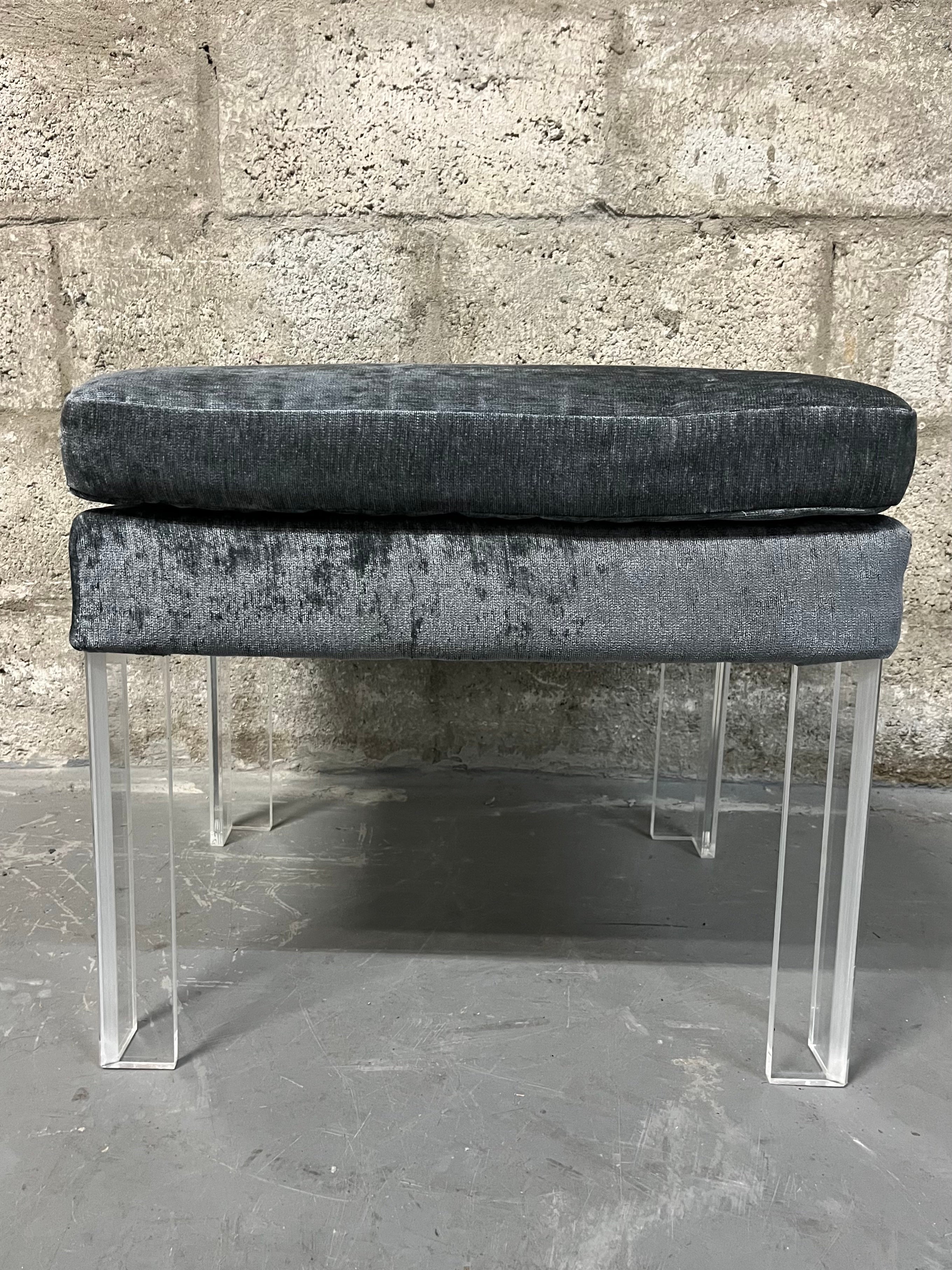Vintage Hollywood Regency Upholstered Lucite Bench in the Karl Springer Style. Circa 1980s
Features angle shaped lucite legs and a newly reupholstered cushion in gray velvety like upholstery. 
In excellent condition with minor signs of wear and age.