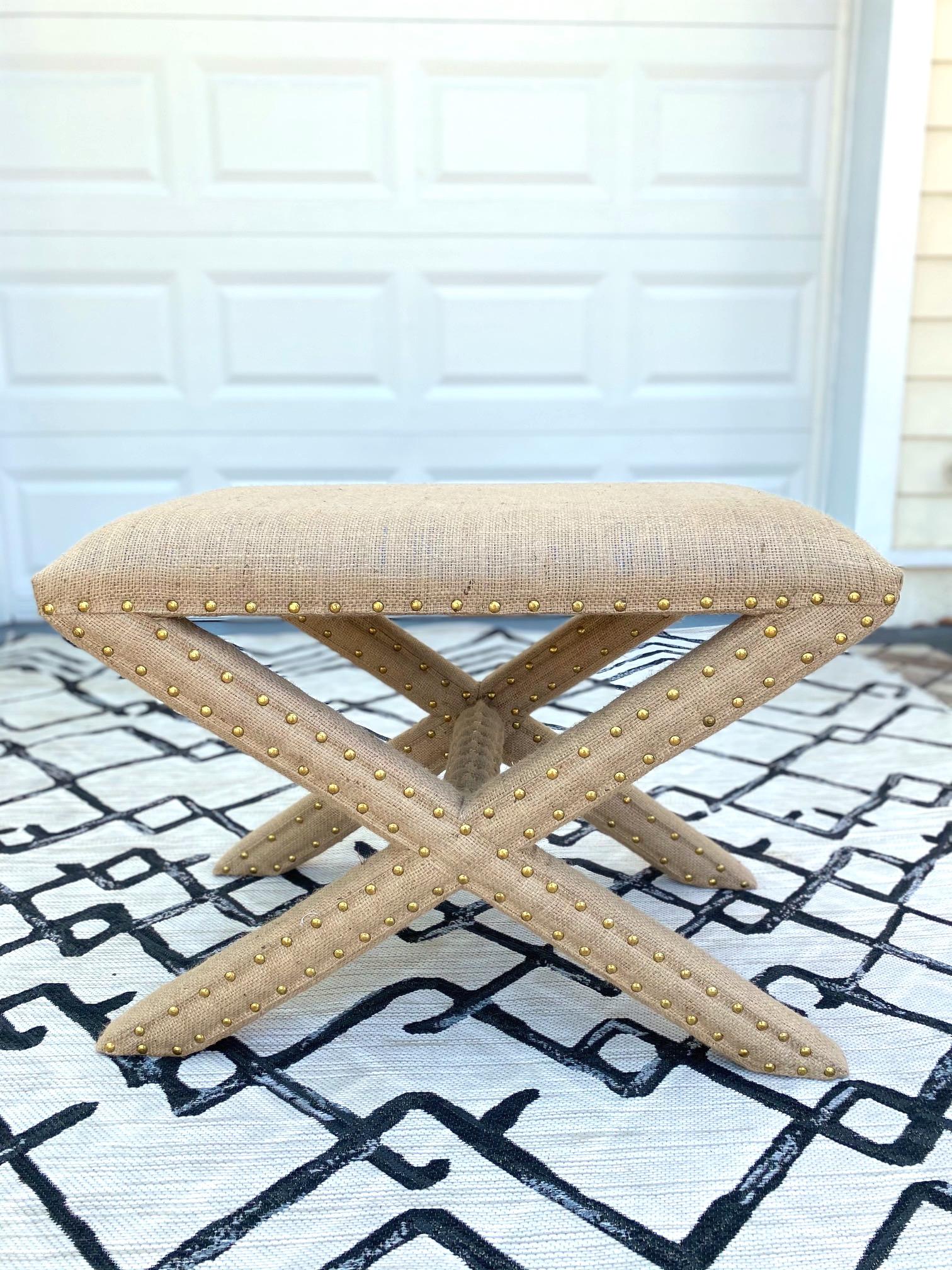 Hollywood Regency style bench with stylized X - Base frame in the style of Billy Baldwin. Completely upholstered in organic jute fiber burlap fabric with gold nail studs throughout.  Makes a chic accent bench for any room.