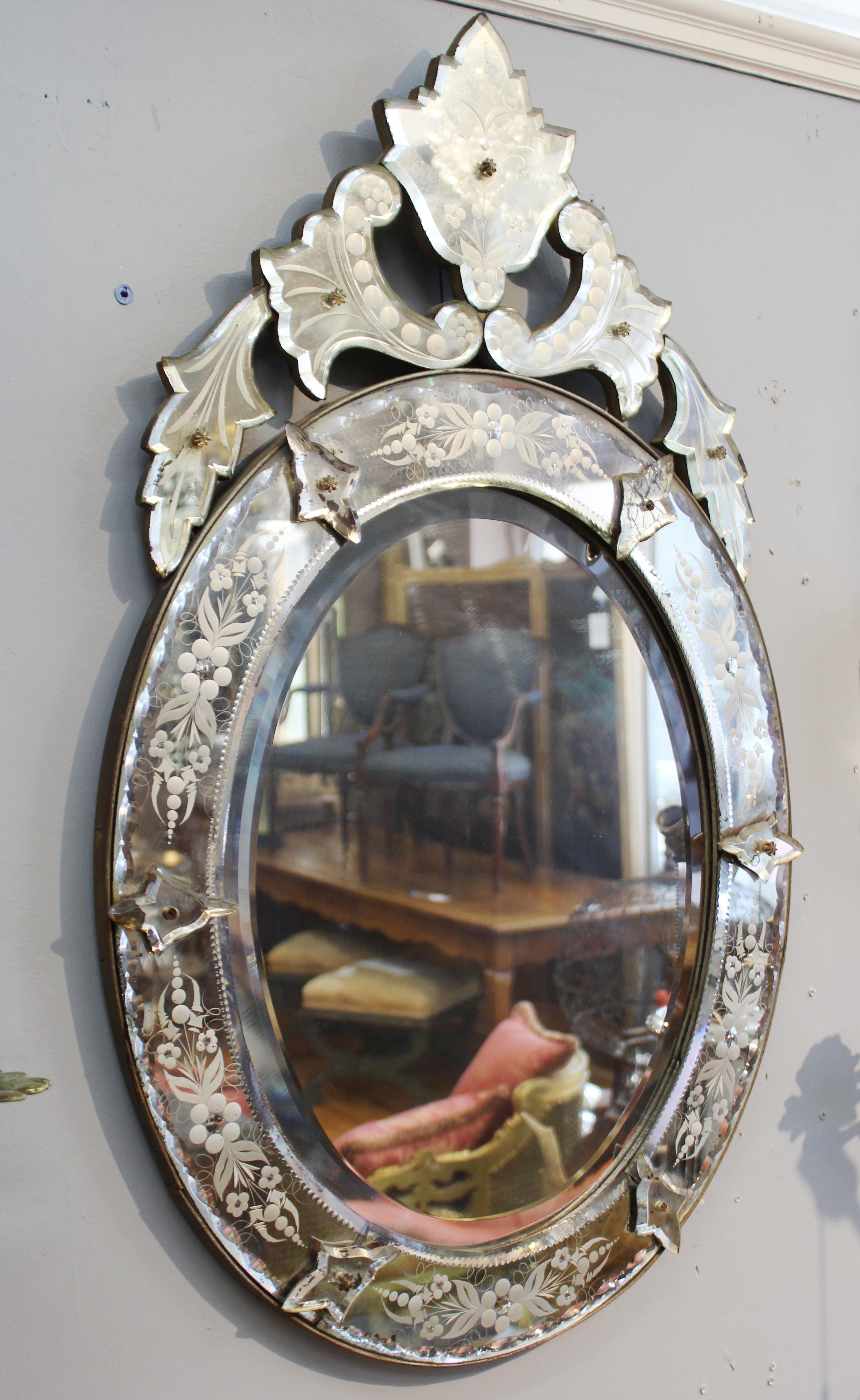 Hollywood Regency Venetian oval shaped wall mirror with beveled and scalloped elements and etched floral decor. The piece is in great vintage condition with age-appropriate wear to the mirror surfaces.