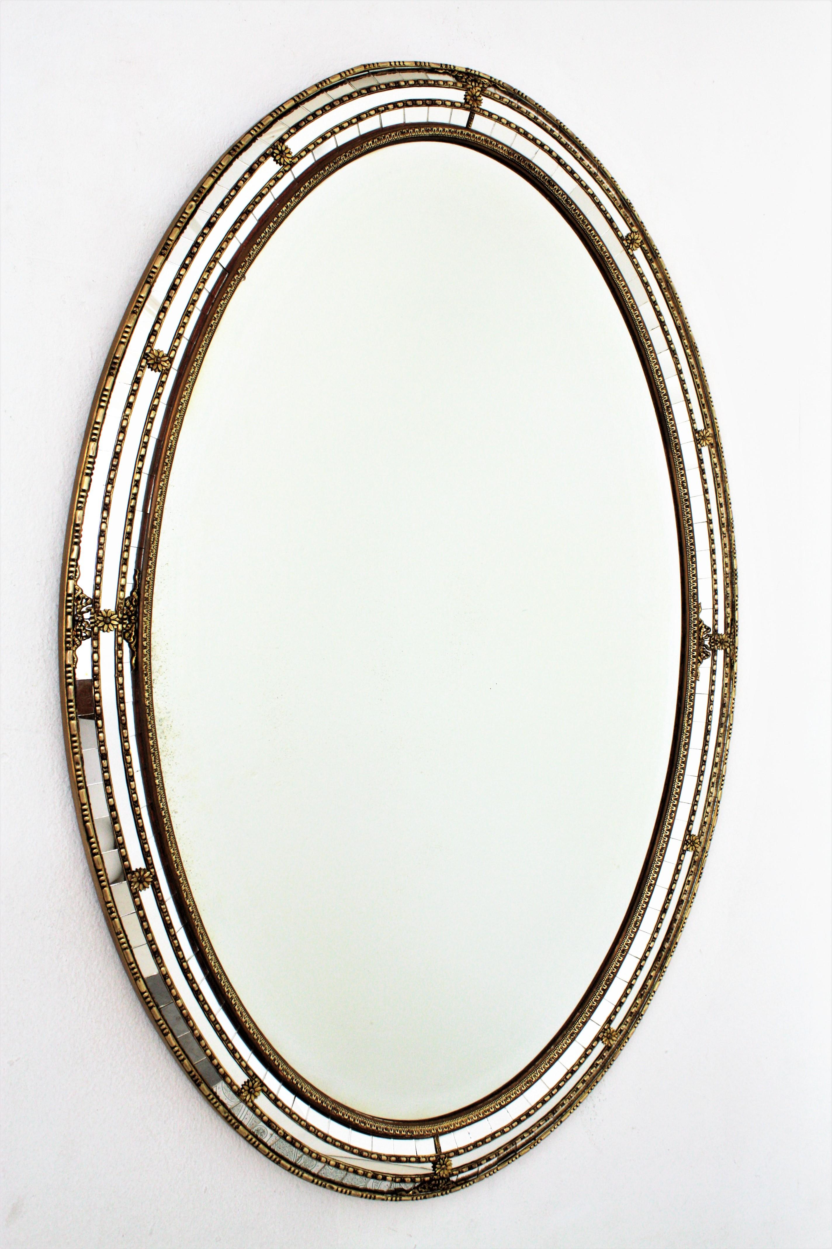 Venetian style Regency modern oval wall mirror with gilt metal accents, Spain, 1950s
This oval mirror is full of beautiful details: It has a beveled central mirror surrounded by a triple mirror mosaic frame cased into a gilt wood structure. The