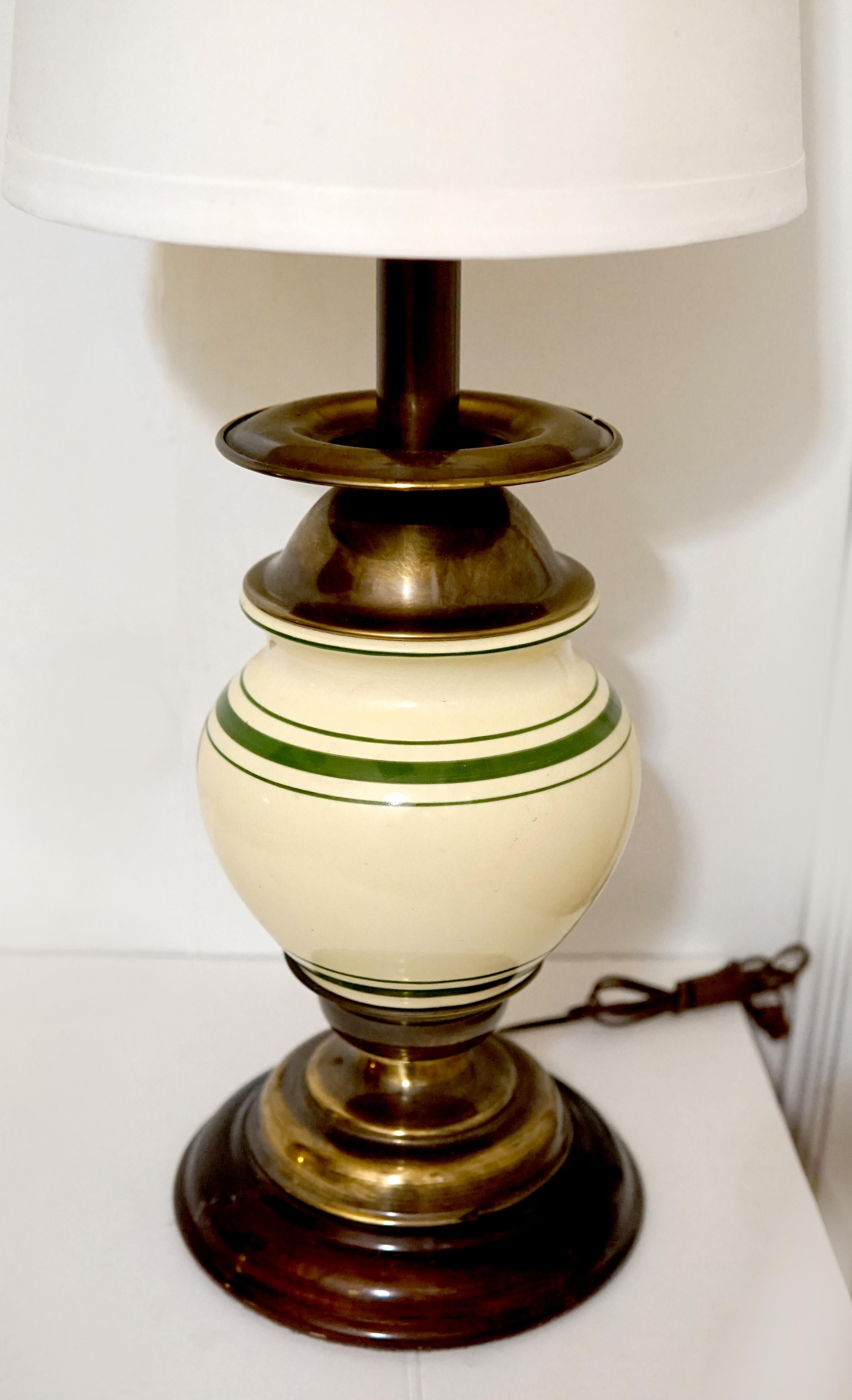 The Stiffel lamp is eggshell color and ovoid  shape. The contrast of the burnished brass and the light tan porcelain is beautiful. The circumference of the lamp is decorated with two green stripes. But a standout feature of this American classic is