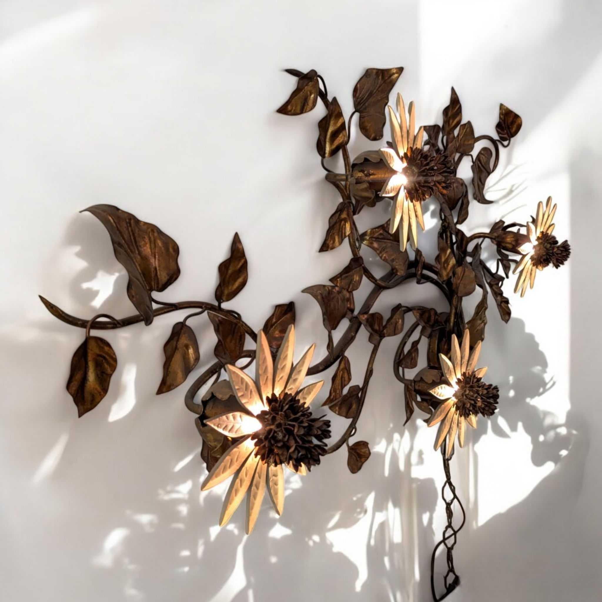 Una caratteristica lampada scultorea a parete nella tradizione Mid-Century Hollywood Regency, realizzata in metallo sagomato a mano e rifinita in ricche tonalità oro e bronzo. Questo pezzo di grande impatto mette in mostra quattro radiosi girasoli o
