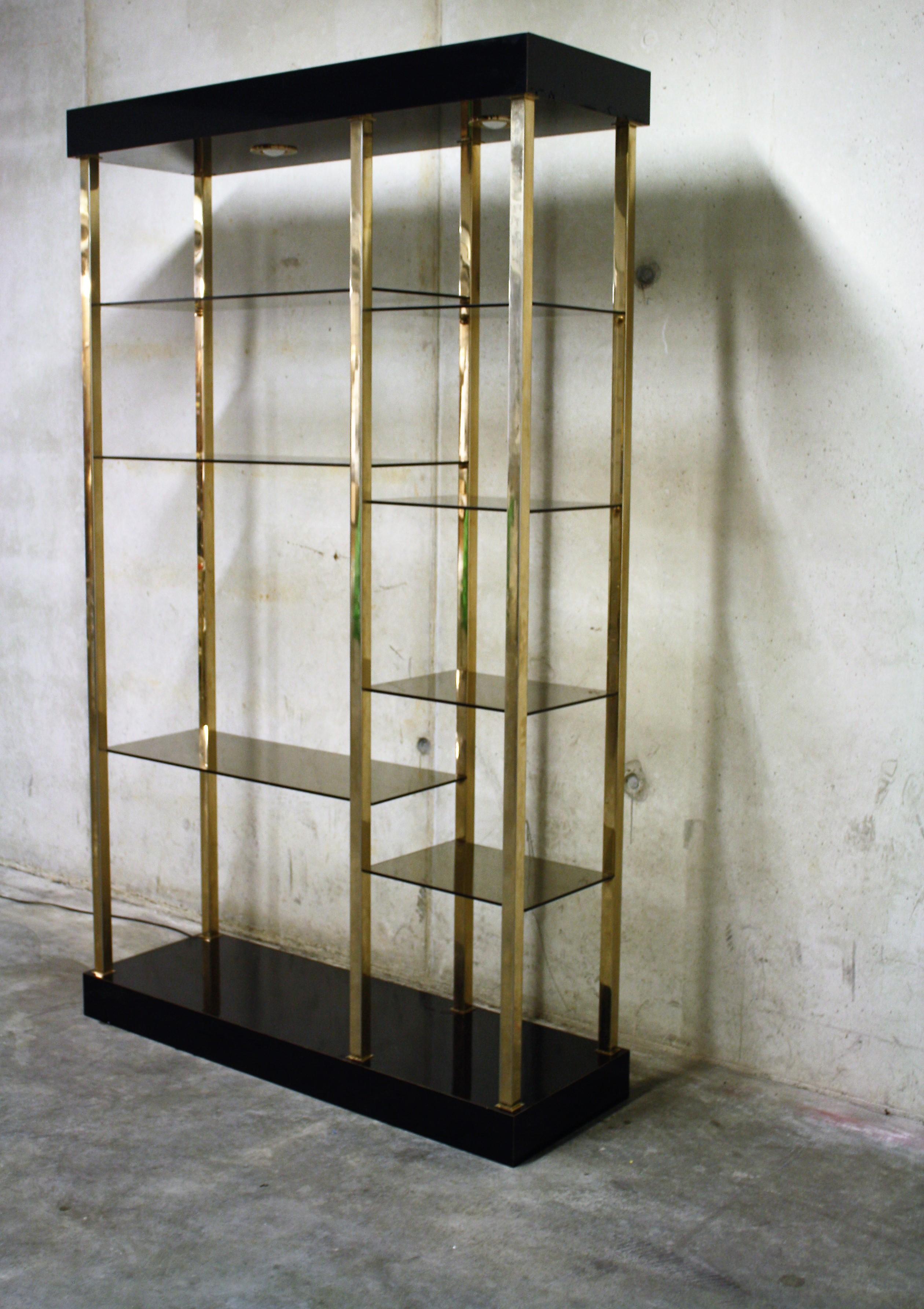 Hollywood regency style wall unit produced by Belgochrom.

This piece is made of 23-karat gold layered metal with a lacquered wooden top and bottom with two lights.

The multi level shelves are made of smoked glass.

The shelve is in good
