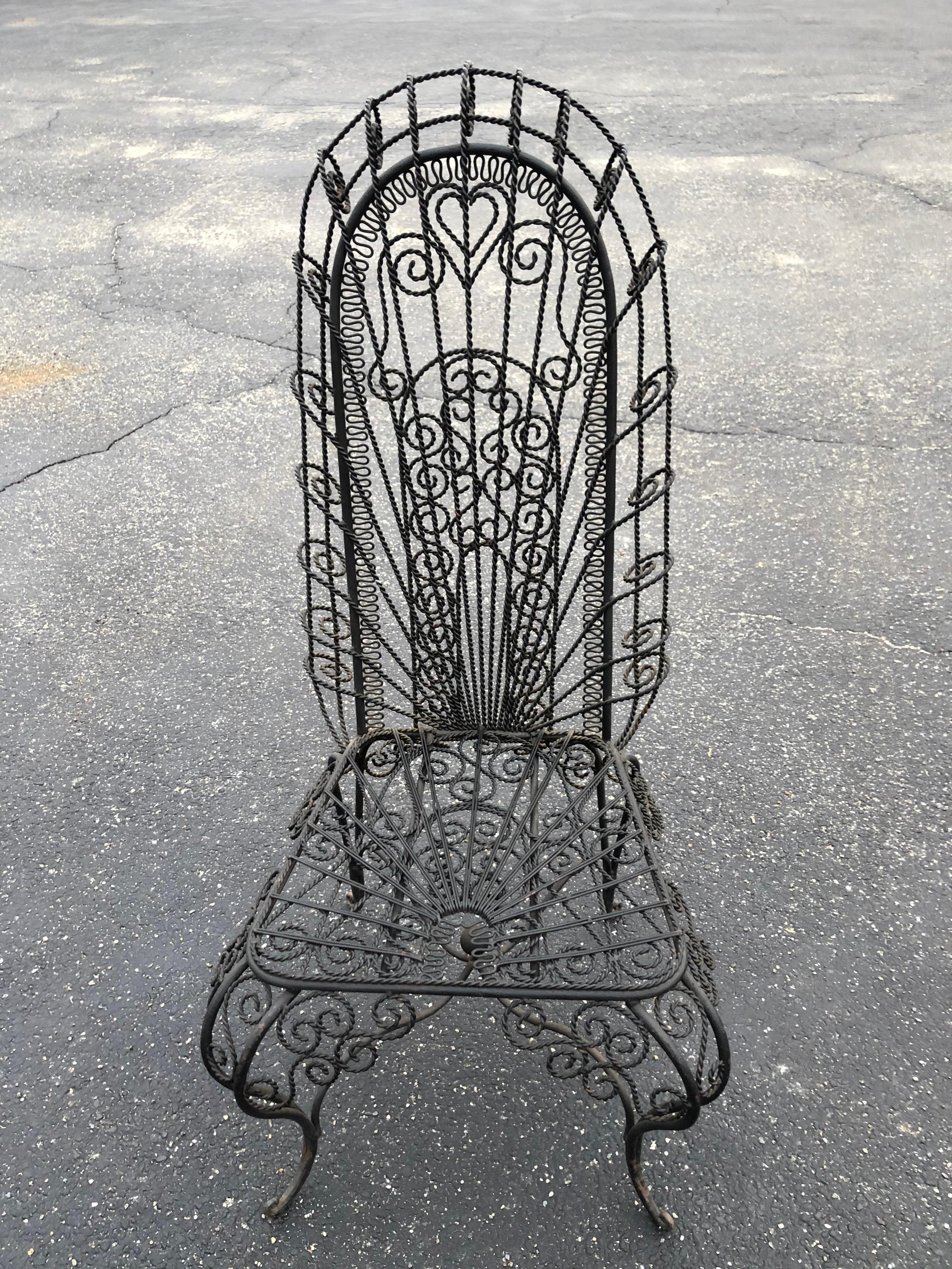 Vintage Hollywood Regency High Back Iron Peacock Chair. Possibly Spanish revival era from the 1960s when Mediterraneum was so in style. Intricate handwrought weaved black iron chair with heart designs. Perfect accent piece for an entryway or patio.