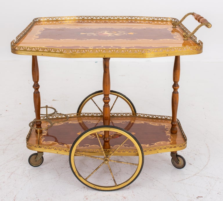 Hollywood regency floral motif mahogany and oak wood marquetry inlaid bar cart with two tiers, two gilt brass wheels, three bottle holders, and two extendable sides. 21.5