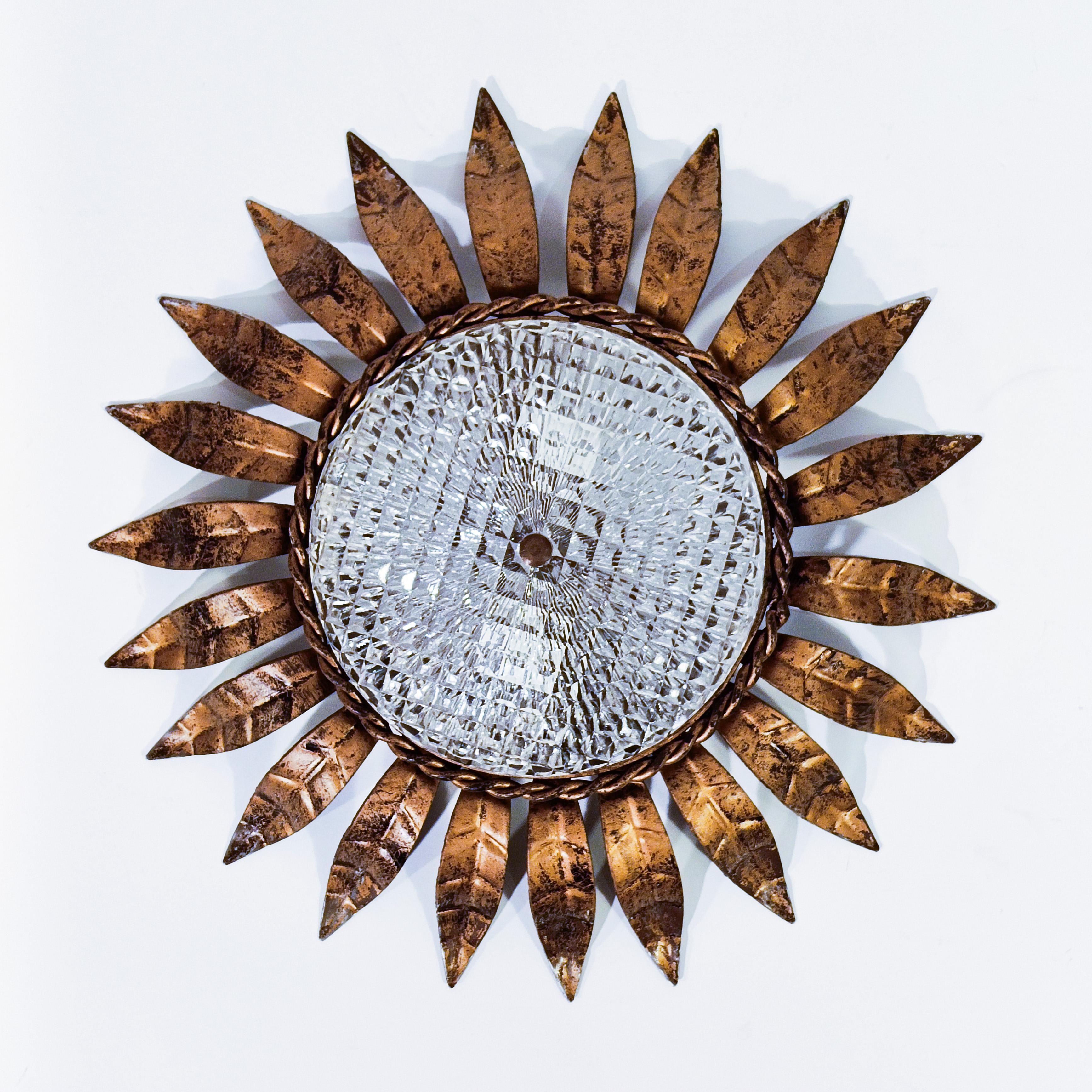 Wrought iron Sunburst style flush mount by Ferro Art (also known as Ferroarte), Spain, 1950s. Metallic body formed by a wrought iron circular base where different leaves are welded as a crown around its perimeter. Molded glass diffuser. Finished in