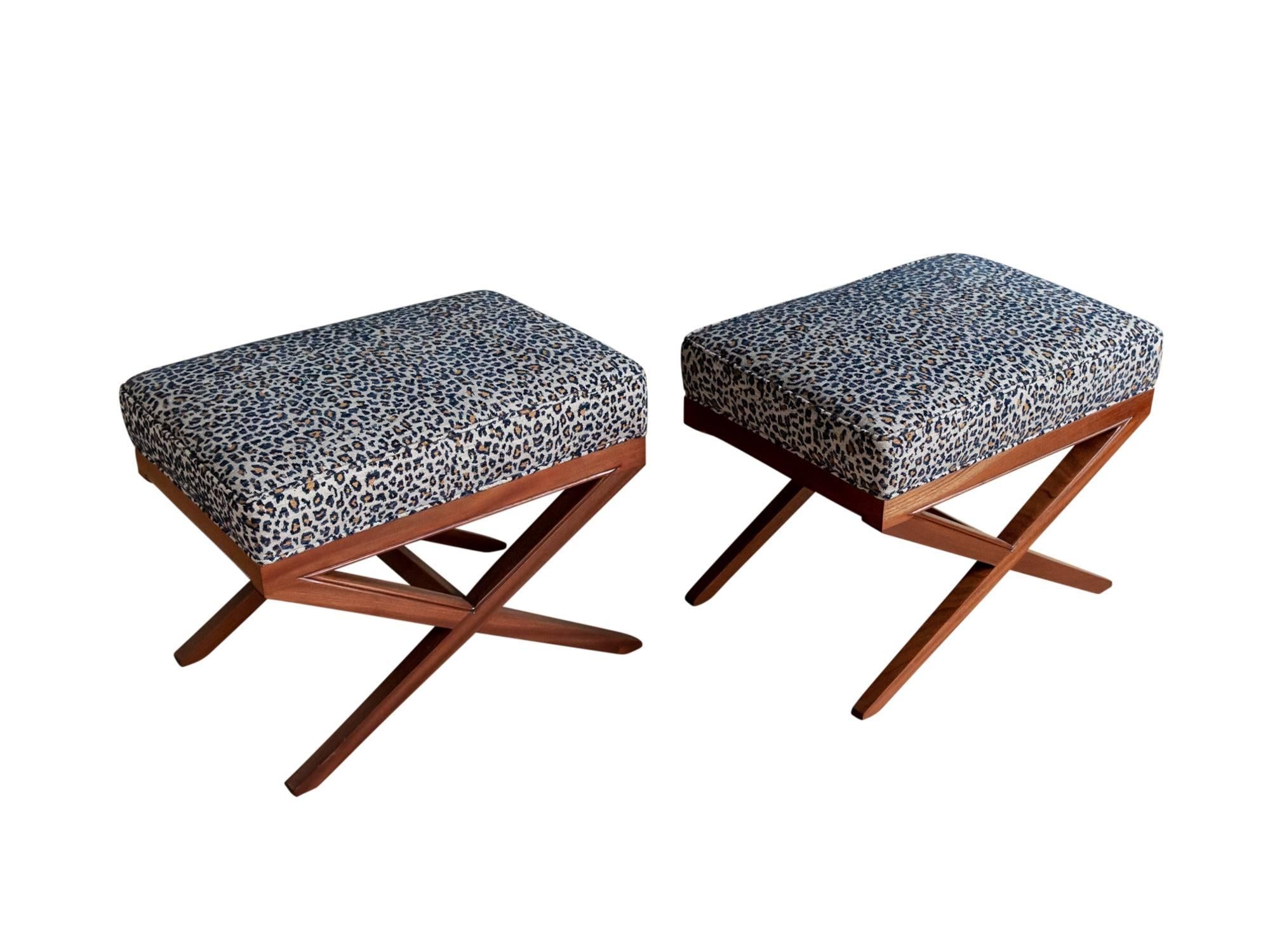 A pair of Hollywood Regency x-base stools or ottomans, circa 1940s or 1950s. Featuring exceptionally well-made mahogany frames supporting upholstered seats or tops. Recently refinished and in excellent condition. Leopard print fabric is also in