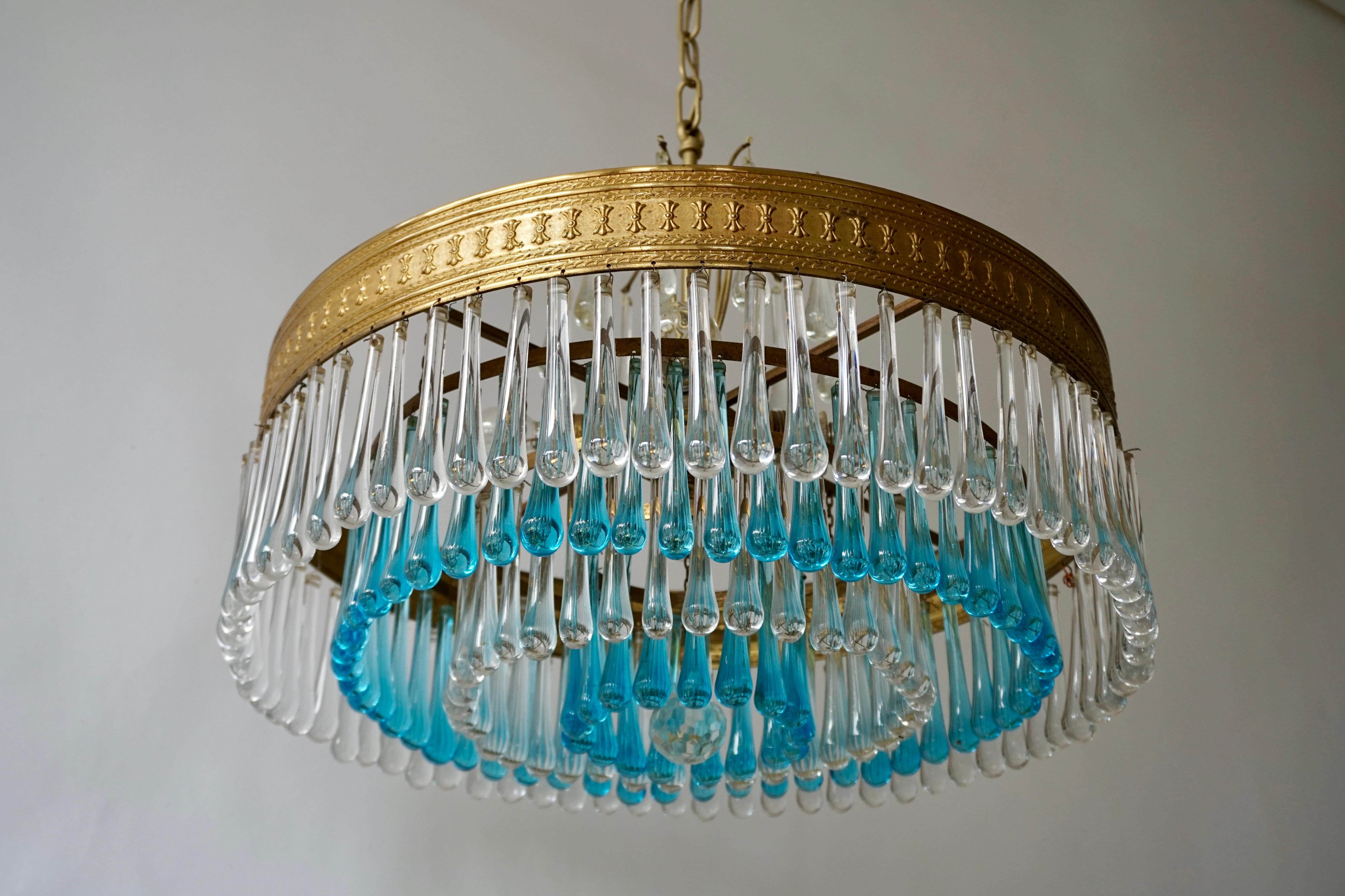 An elegant flushmount chandelier with blue and transparent crystal teardrop glass segments in a radial pattern. The result is a very sparkling effect typical of Hollywood style and glamour. The fixture is brass and the glass is hand blown.
The