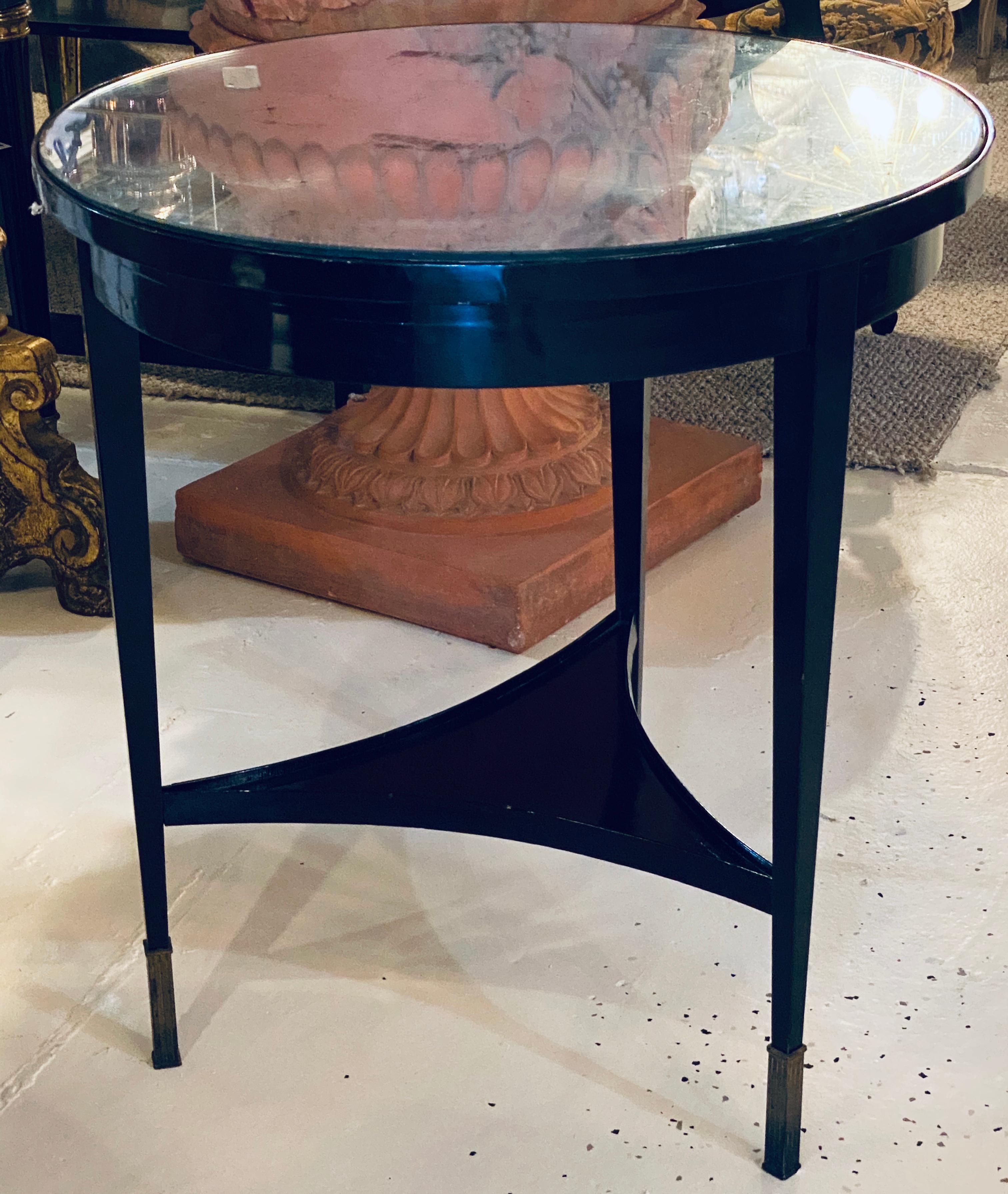 An ebonized silver gilt mirror top center or end table. On bronze sabots having tapering legs with a lower triangular inverted shelf this sleek and stylish end table is certain to add that Hollywood Regency charm that is highly sought after.