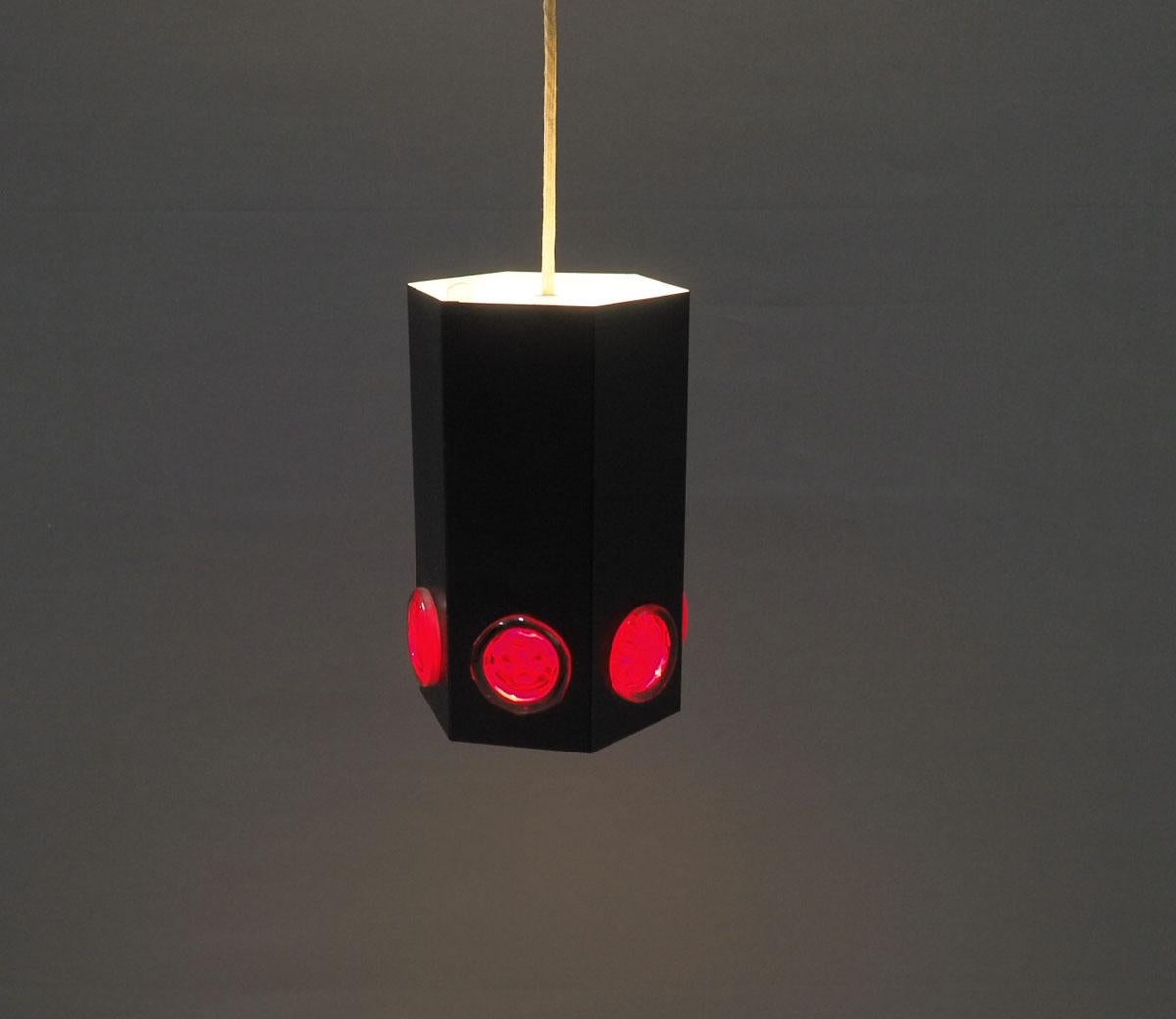  Rare lampe en forme de cylindre en métal peint par poudrage noir des années 1960 produite par Holm Sorensen.

La lampe a 6 coins et un cercle de verre rouge sur chaque surface en bas.

L'intérieur est blanc, la lampe donne un effet de lumière