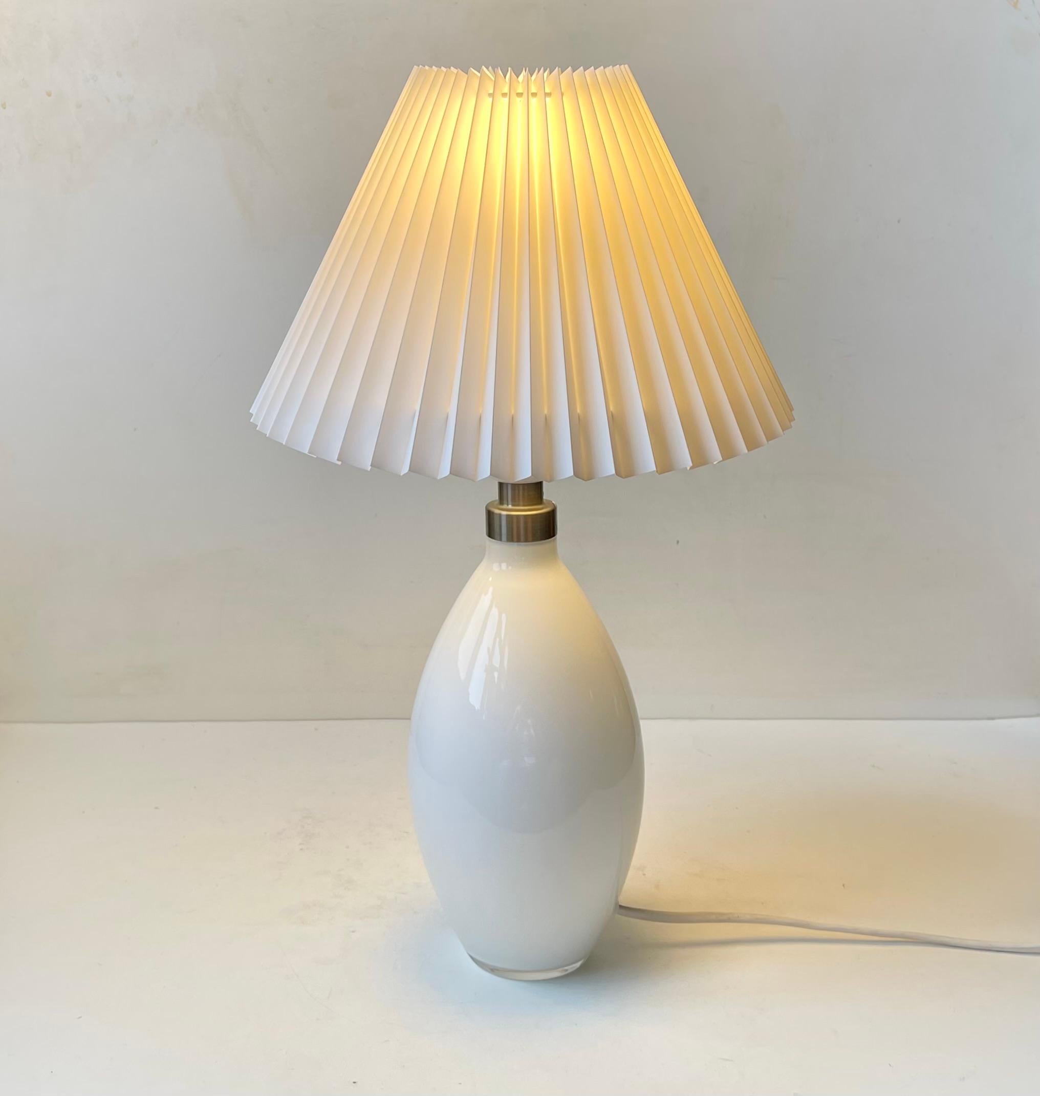 Stylish hand-blown table lamp in white opaline glass. Designed by Peter Svarrer and manufactured by Holmegaard in Denmark during 1990s or early 2000s. It comes with a new fluted white Danish shade. Measurements: H: 44 cm, Diameter: 27 cm (shade). 
