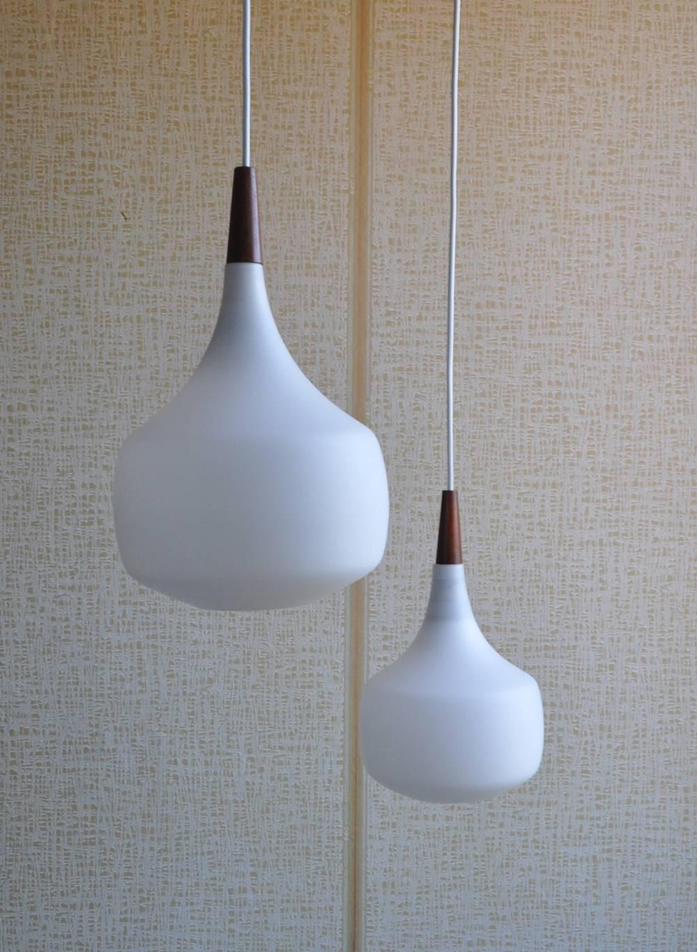 Scandinavian midcentury minimalisme. Clean sharp lines and forms. 
Holmegaard hanging lamp from Denmark, teak and opaline glass.
Signs of wear consistent with age and use.

Measures: Height 33.5 cm, diameter 21 cm.
Height 29.5 cm, diameter 17.5