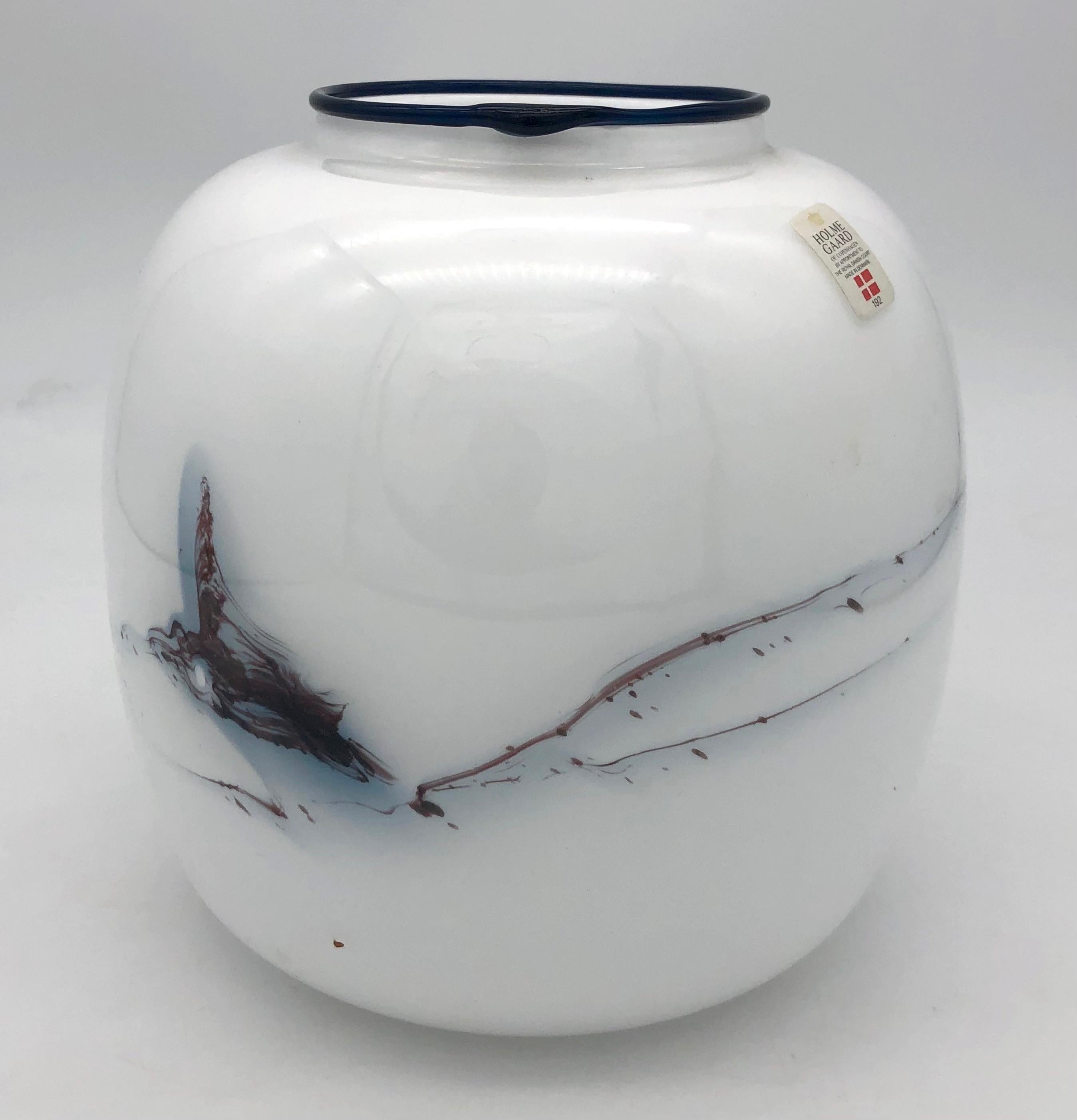 This opaque white glass vase with a black rim is decorated in the glass with an abstract motive. 
The vase has retained it's original paper label.