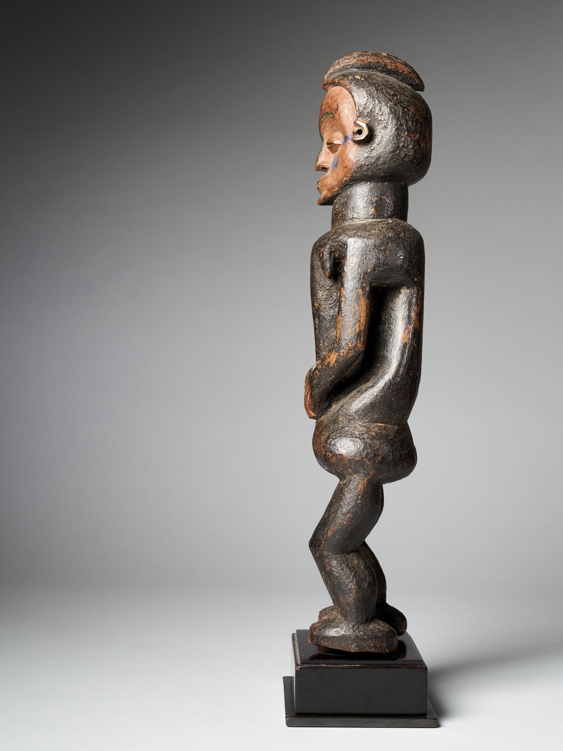 The Cult statue Mvunzi, represents an Ancestor carved with slightly bent legs and her hands joining the abdomen. The crested hairdo, proportioned body, scarified face with coffee-bean eyes, bent legs, and blue polychrome characterizes their Holo’s