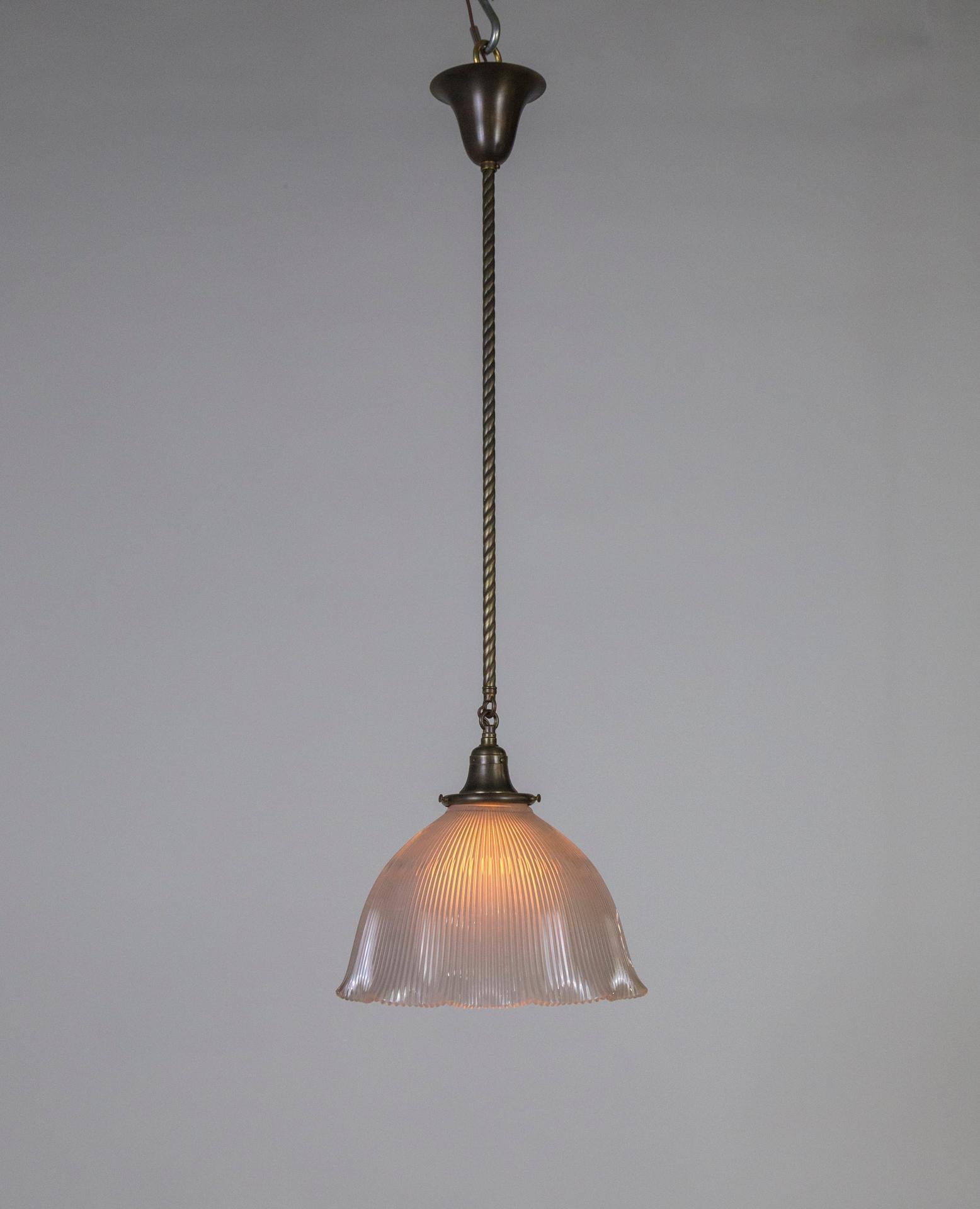 A pendant light with an antique (c. 1910), bell flower shaped, holophane glass shade with an elegant, ruffled bottom; with a switch at the socket, hung with antiqued tone brass rope stem. Paired with matching shade holder and canopy. Newly made and
