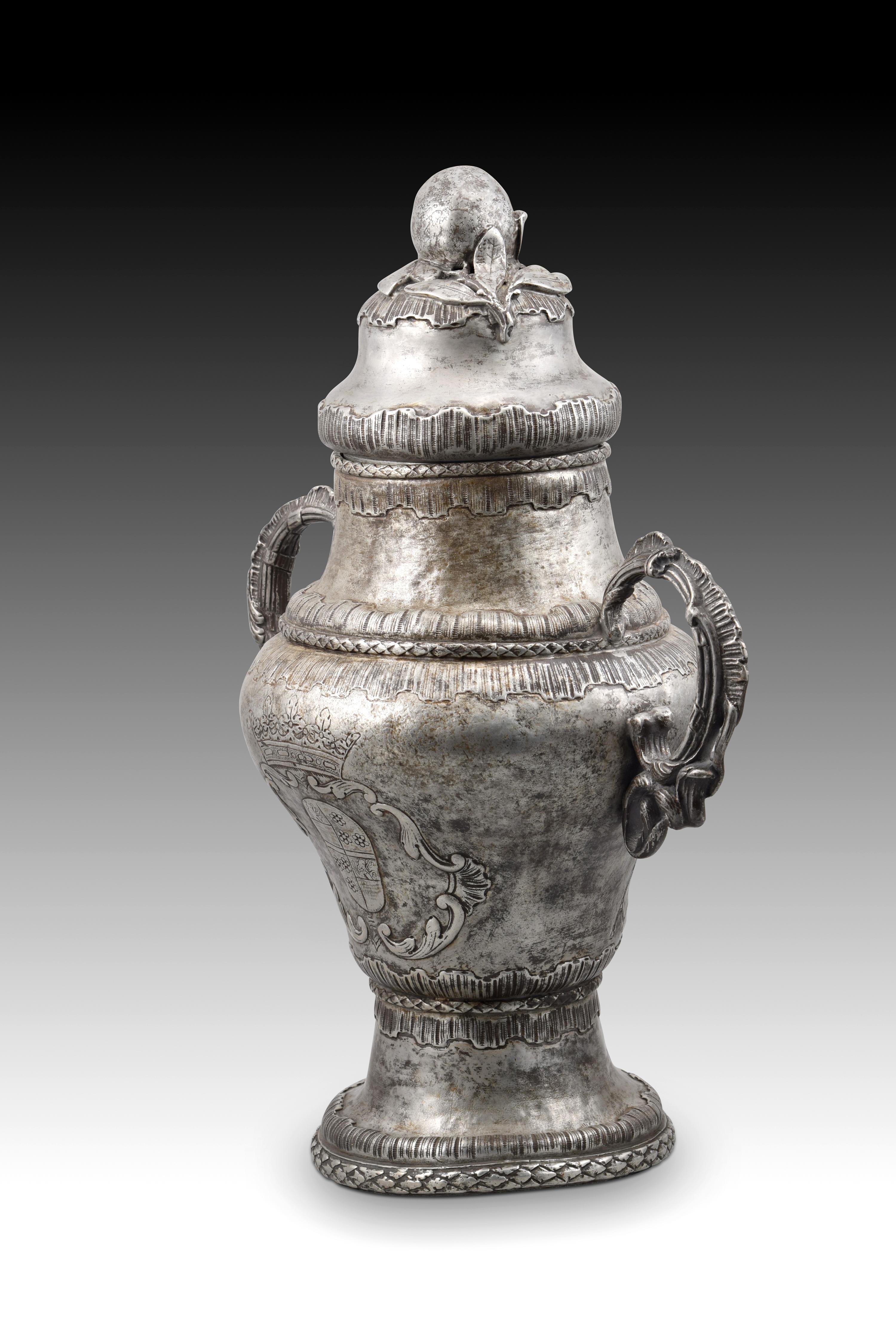 Santos Oils container. Pewter. Century XVIII. 
Container made of pewter that has a foot, a body with curves, two handles and a lid. Its exterior decoration shows a clear influence of the European Rococo style of the 18th century (note the seed