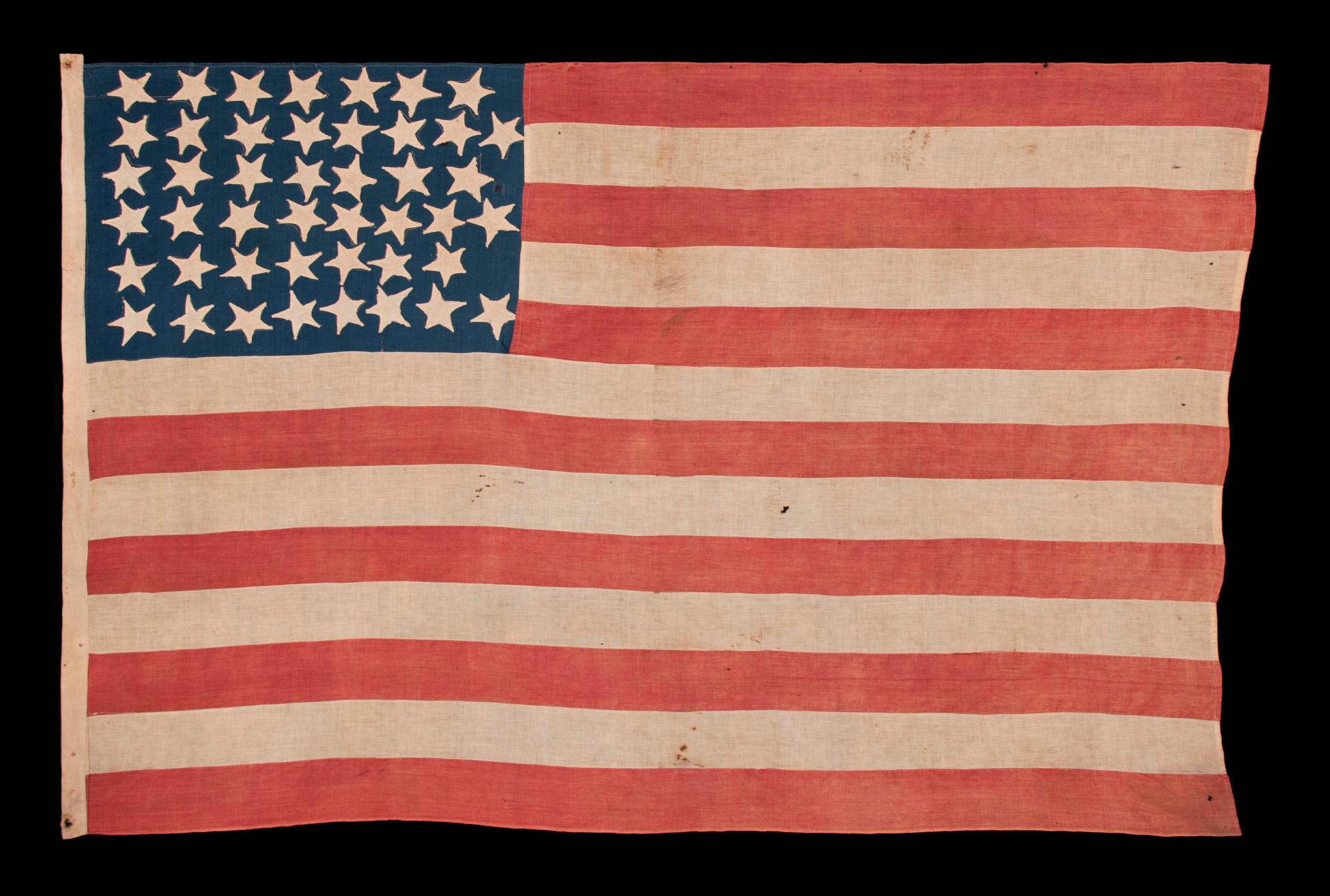 HOMEMADE, ANTIQUE AMERICAN FLAG WITH A TINY CANTON RESTING ON THE 6TH STRIPE AND AN EXTREMELY FOLKY PRESENTATION OF 45 STARS IN A “NOTCHED” PATTERN THAT MIGHT BE UNIQUE TO THIS EXAMPLE; REFLECTS THE ERA WHEN UTAH WAS THE MOST RECENT STATE TO JOIN