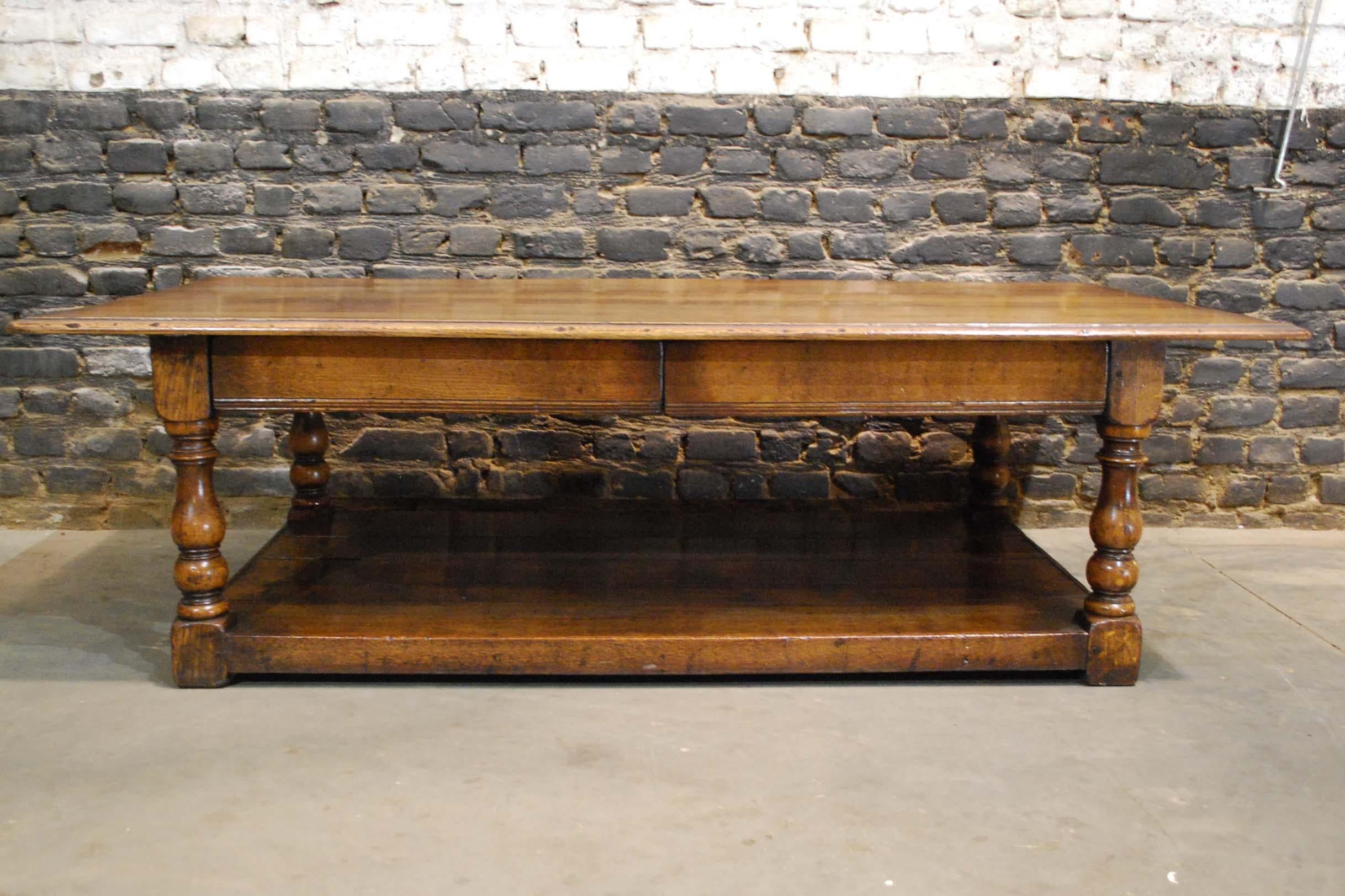 A beautiful coffee table, custom made in the United Kingdom.
It is completely made in the finest quality solid oak. The table has four turned slender baluster legs.
The skirt houses two hidden oak drawers. Below sits a planked pot board. The