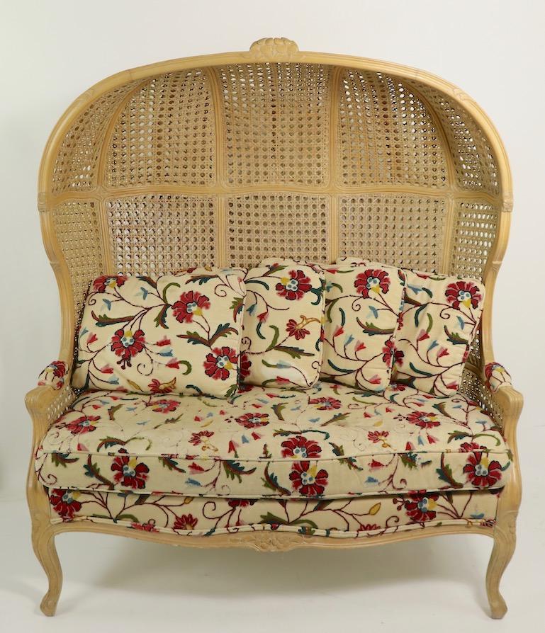 Unusual hooded loveseat size sofa probably American made in the French style. The sofa is in very good structural condition, the crewel work upholstered fabric shows significant wear and staining. Decorative and fun sofa, in cool boho chic