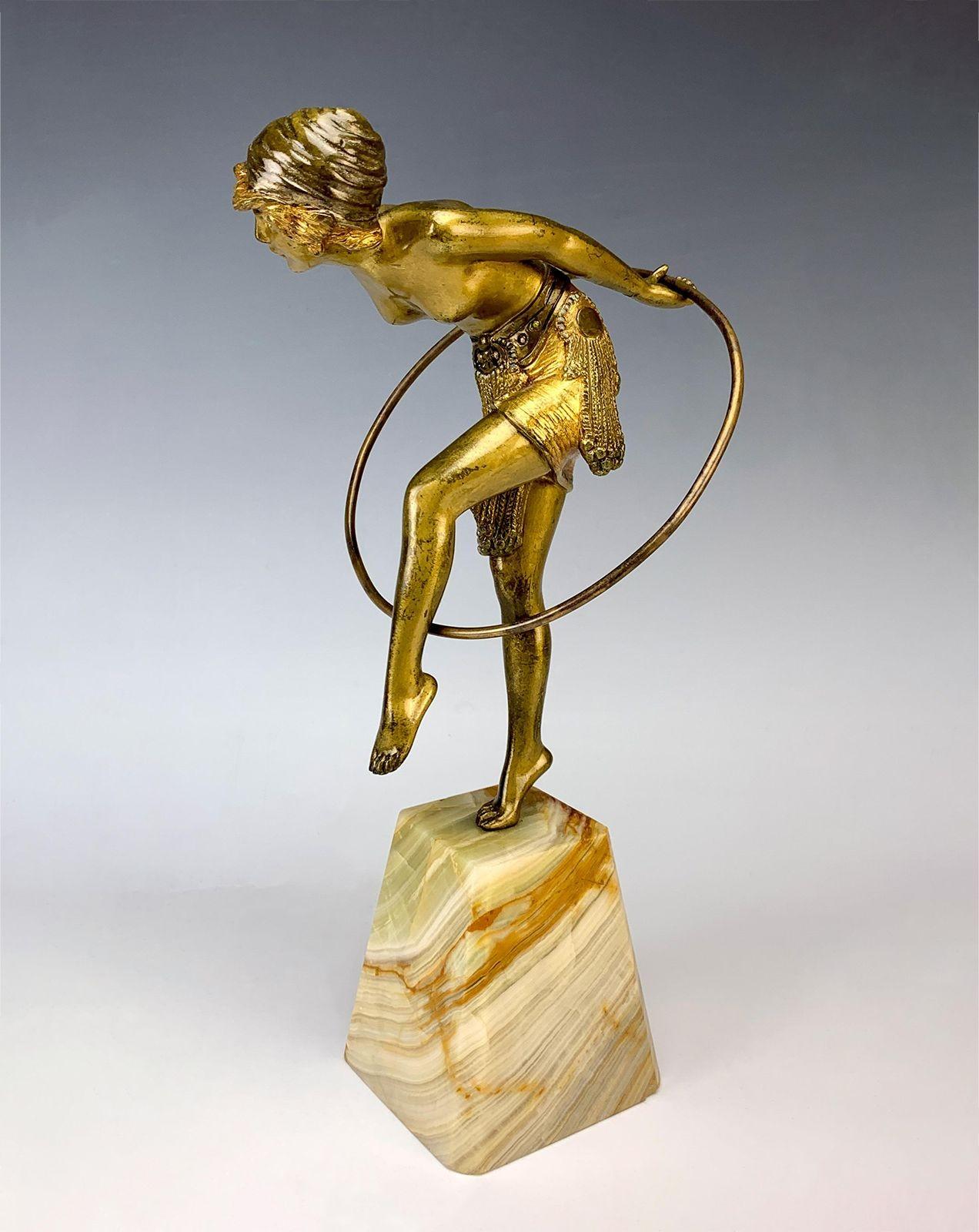 This Demétre Chiparus gilt bronze sculpture is a charming representation of movement and grace. It depicts a hoop girl dancer elegantly twirling her hoop around her body. The sculpture is standing gracefully on a tapering veined onyx base which