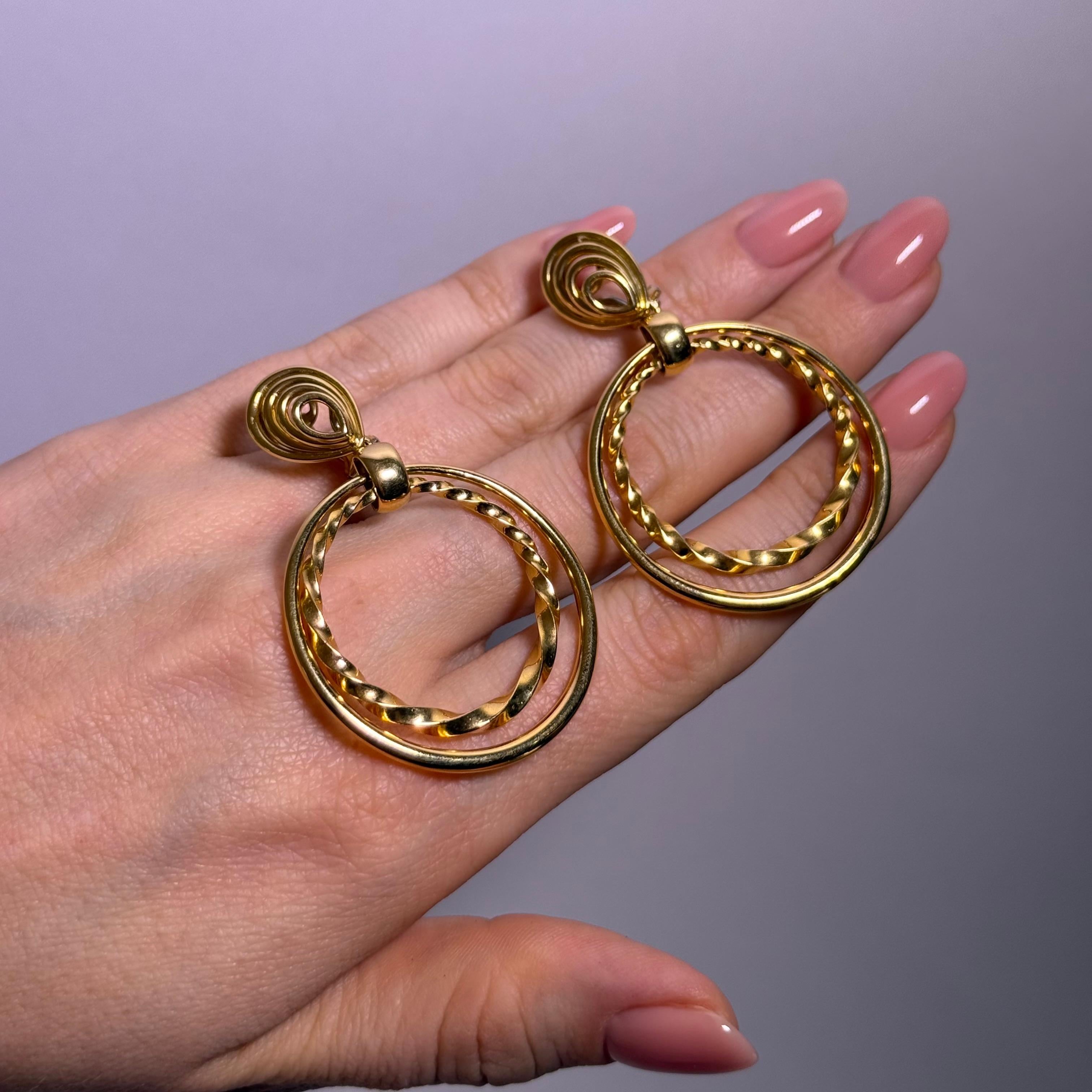 Crafted by Gübelin in luxurious 18 karat gold, these elegant hoop earrings feature a refined contrast. 

One hoop boasts a sleek, polished finish, while the other playfully twists in a graceful, twirled design. United in a single piece, they strike