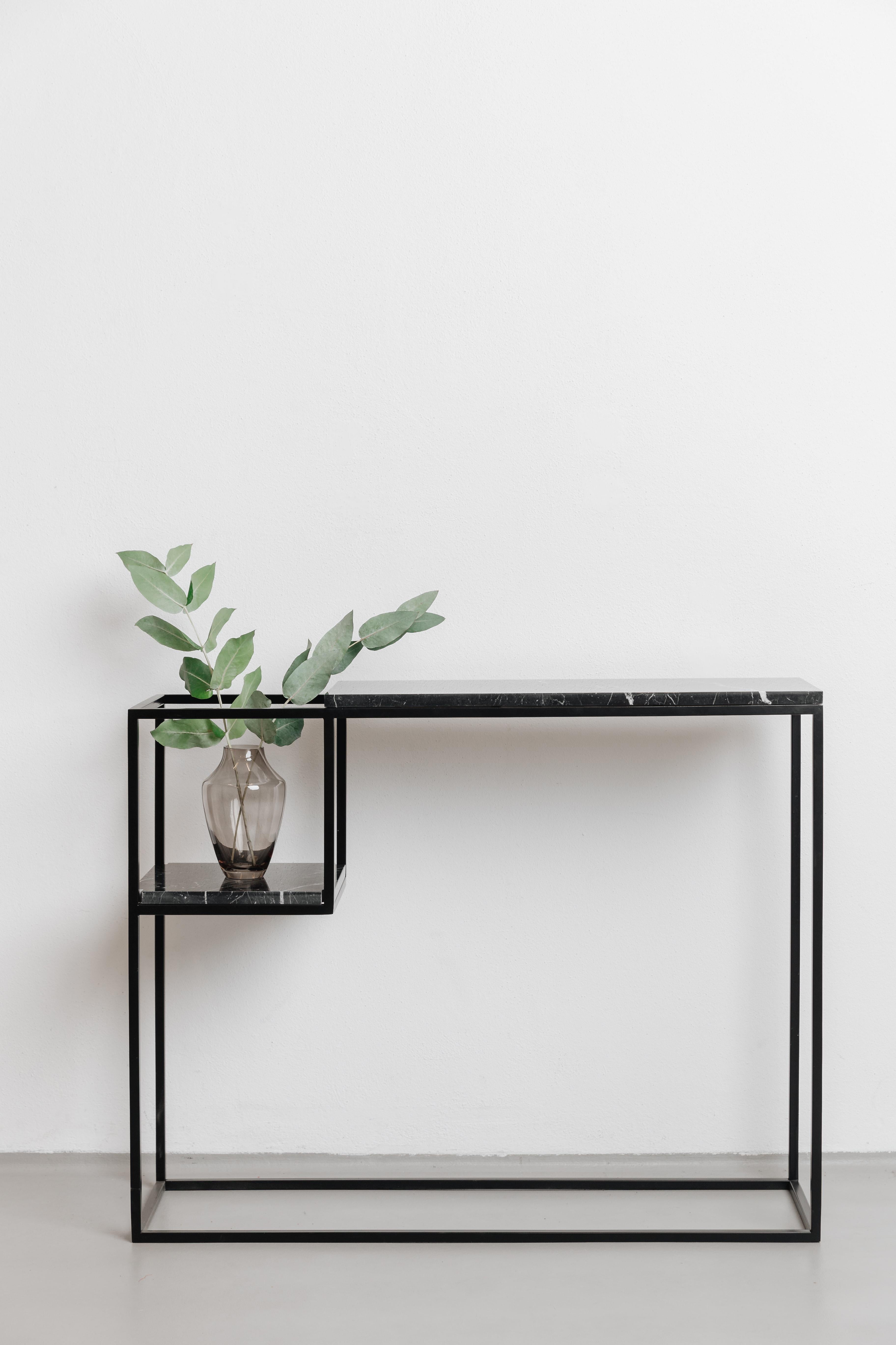 Die Konsole HOP MAXI hat eine Marmorplatte auf einem schwarzen Stahlrahmen. Sie wird in Ihrem Flur, Wohnzimmer oder Schlafzimmer großartig aussehen. Das abgesenkte Regal ist der perfekte Platz für Blumen oder Bücher und bietet eine unkonventionelle