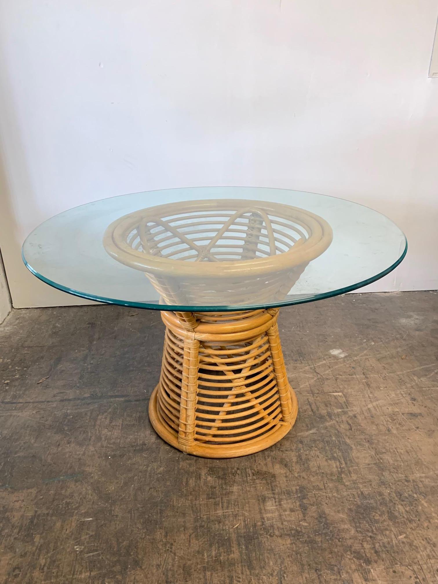 Pedestal dining table features horizontal rattan ring construction and a glass top. Unique hourglass shape. Very good condition.