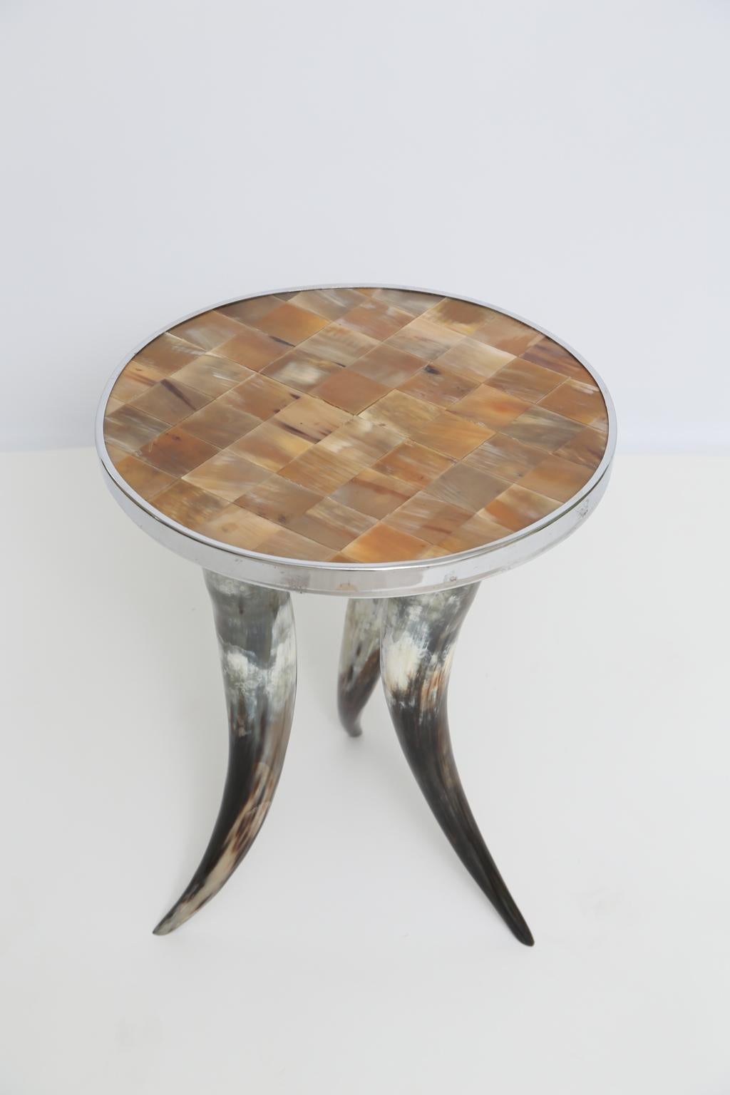 Side table, having a round top of patchwork Horn tiles resembling tortoise, with chrome border, raised on a trio of steer horns as legs.

Stock ID: D 2477.