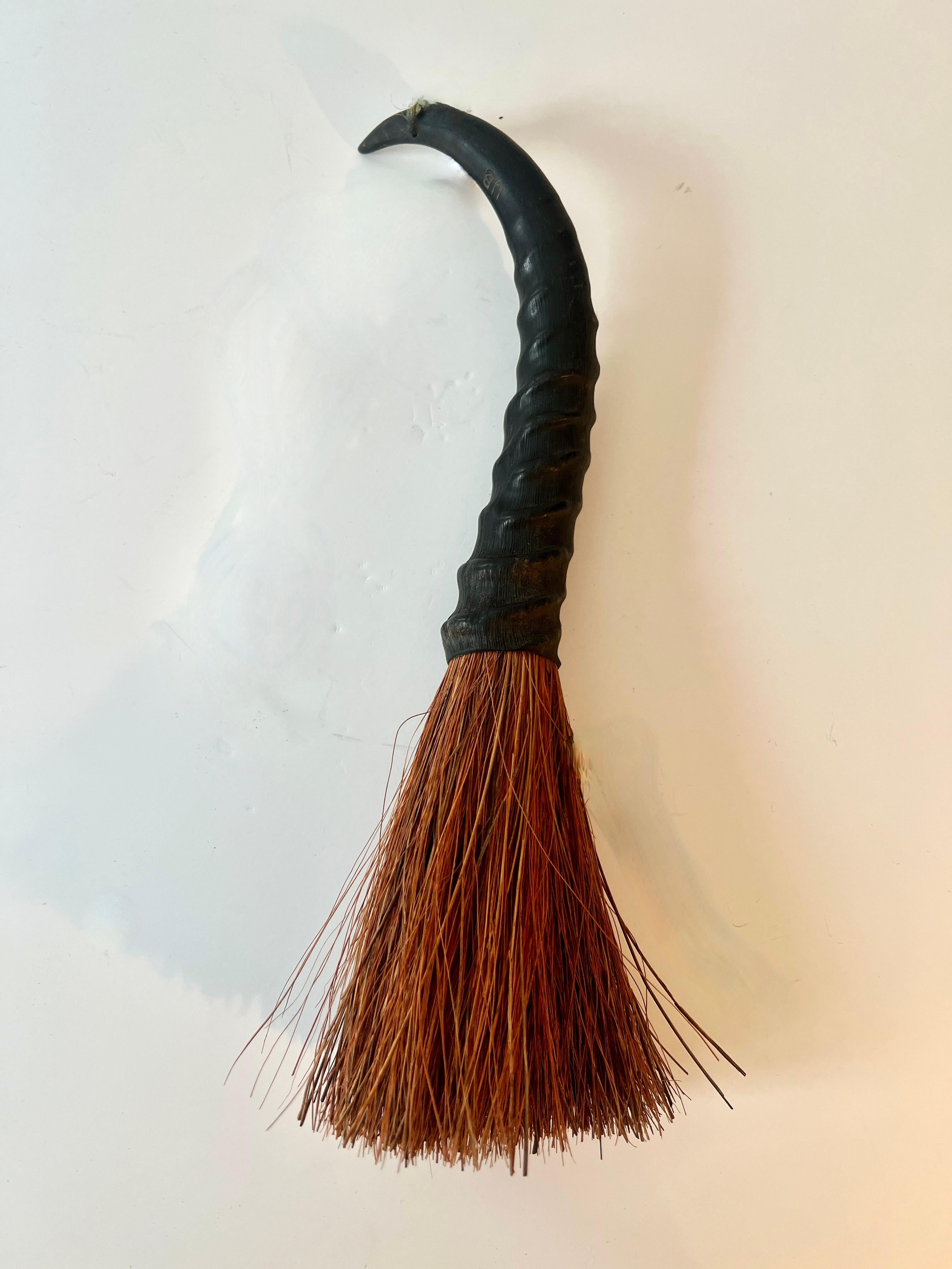 A small broom, or whisk Broom.  Perfect for cleaning up small area of dirt, ash or crumbs from the table, fireplace or small pet debris.  Also works perfectly as a decorative item.

The horn could be resin, but definitely has the look or horn and
