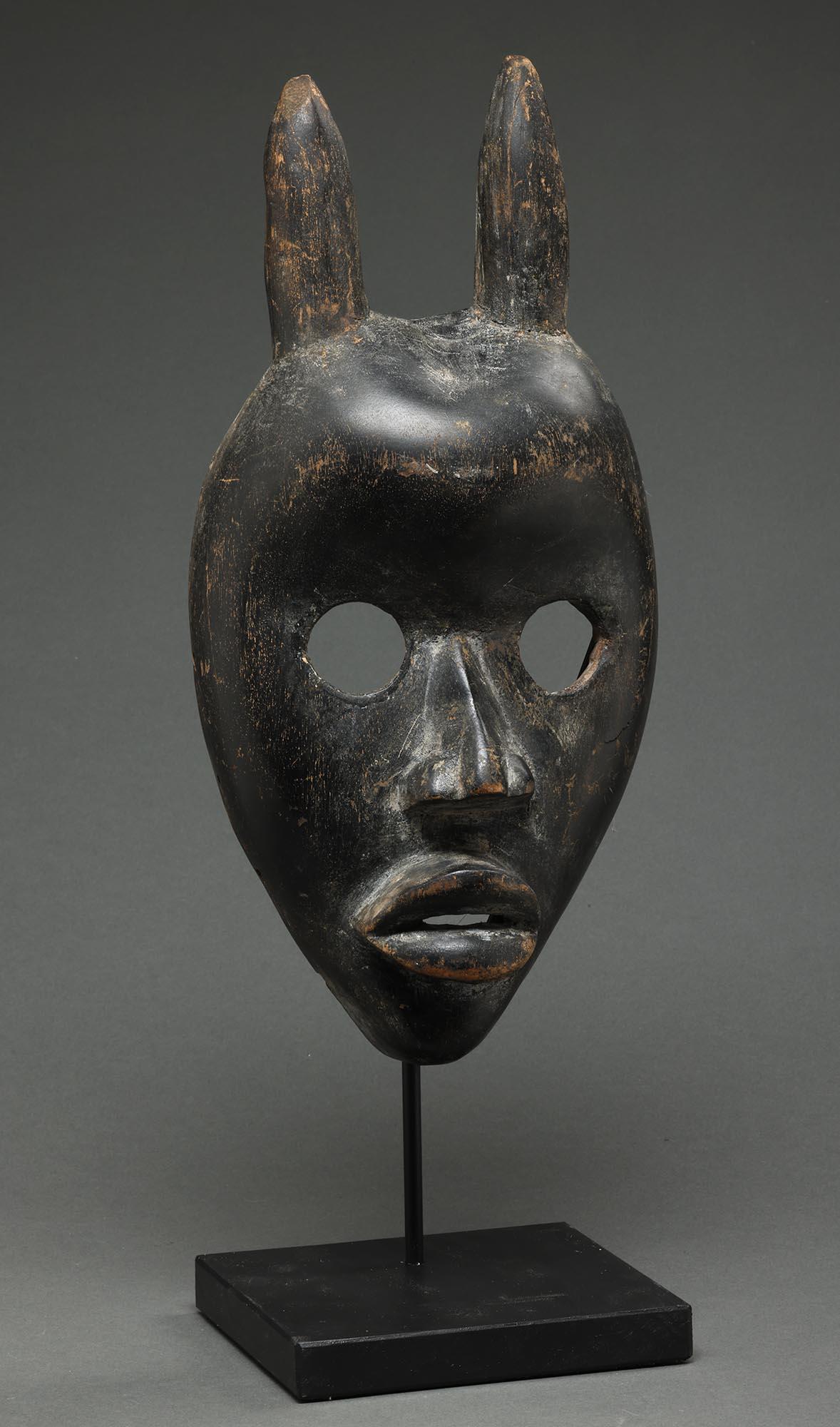 Geschnitzte Antilopenmaske aus geschwärztem Holz mit Horn - Menschenmaske Dan People Elfenbeinküste, Afrika.  Zwei vertikale Hörner, die wahrscheinlich eine junge Antilope darstellen, große offene runde Augen und vorspringende Lippen.

Es ist in