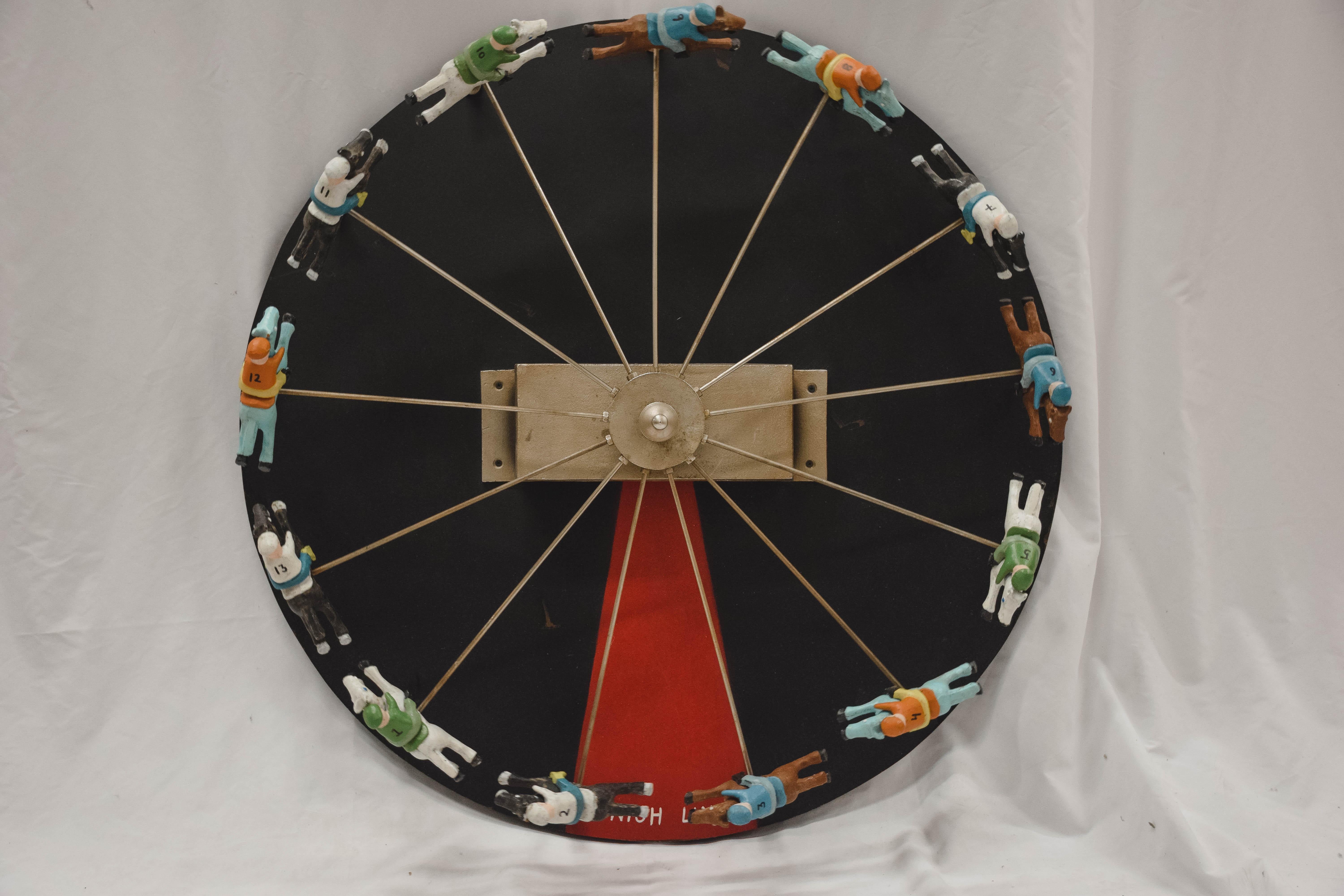 Nous adorons cette roue de jeu de course avec cheval et jockey et nous savons que vous le ferez aussi. L'œuvre présente treize combinaisons de chevaux et de jockeys en métal coulé:: peints en couleurs:: sur les rayons d'une roue en métal. Ils