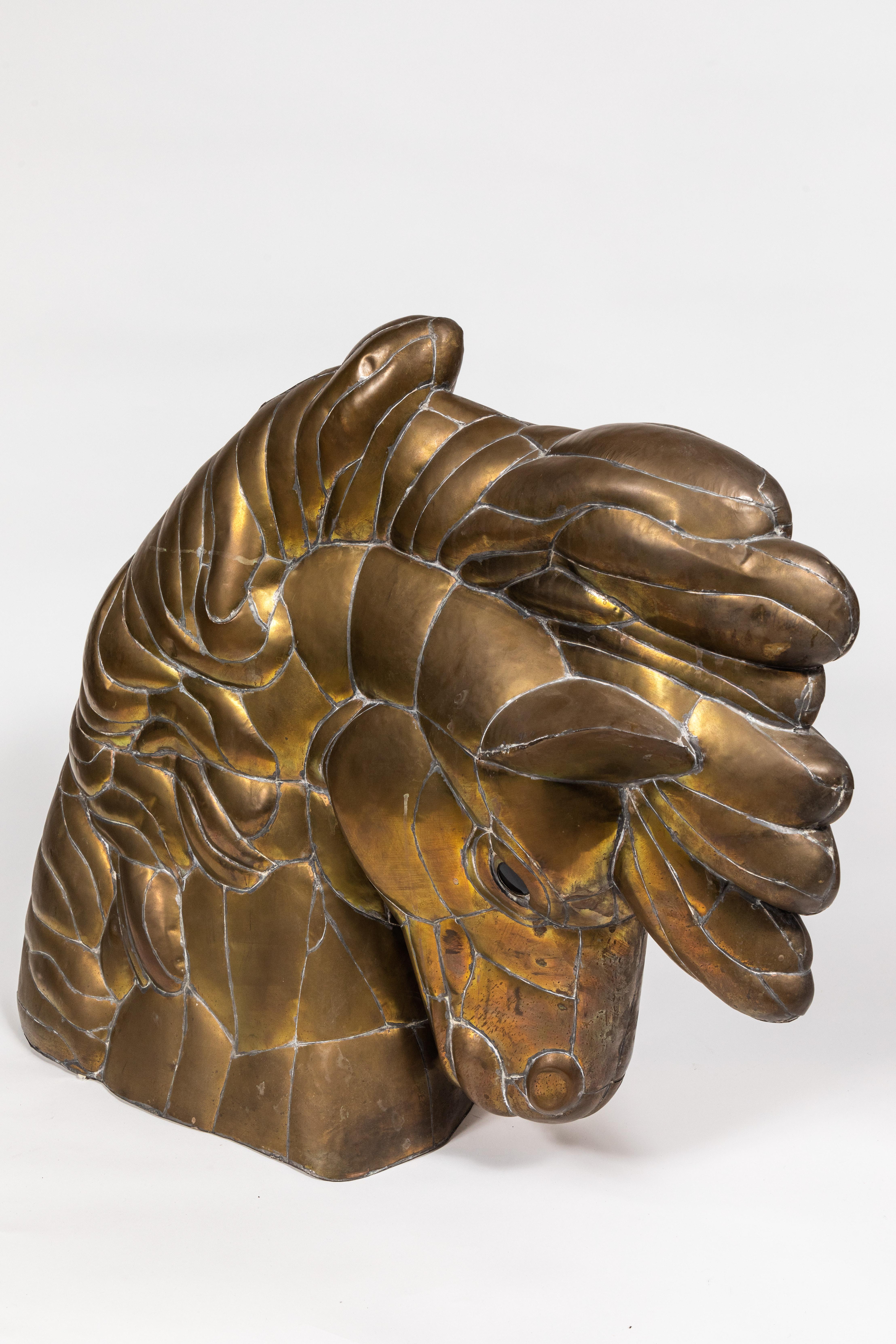 This expressive horse head sculpture in pieced and welded brass features flared nostrils, a flowing mane, and glass eyes. It rests on its finished and closed base. Hollow. No signature found.