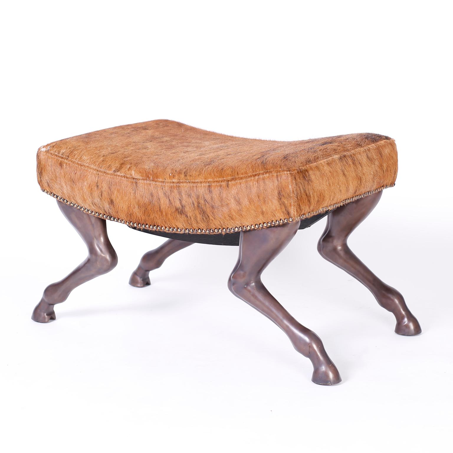  Horse Hide Bench by Theodore Alexander Striking bench or footstool with a concave cushion upholstered in horse hide and bordered with brass tacks over horse form metal legs with a bronze like patina.
