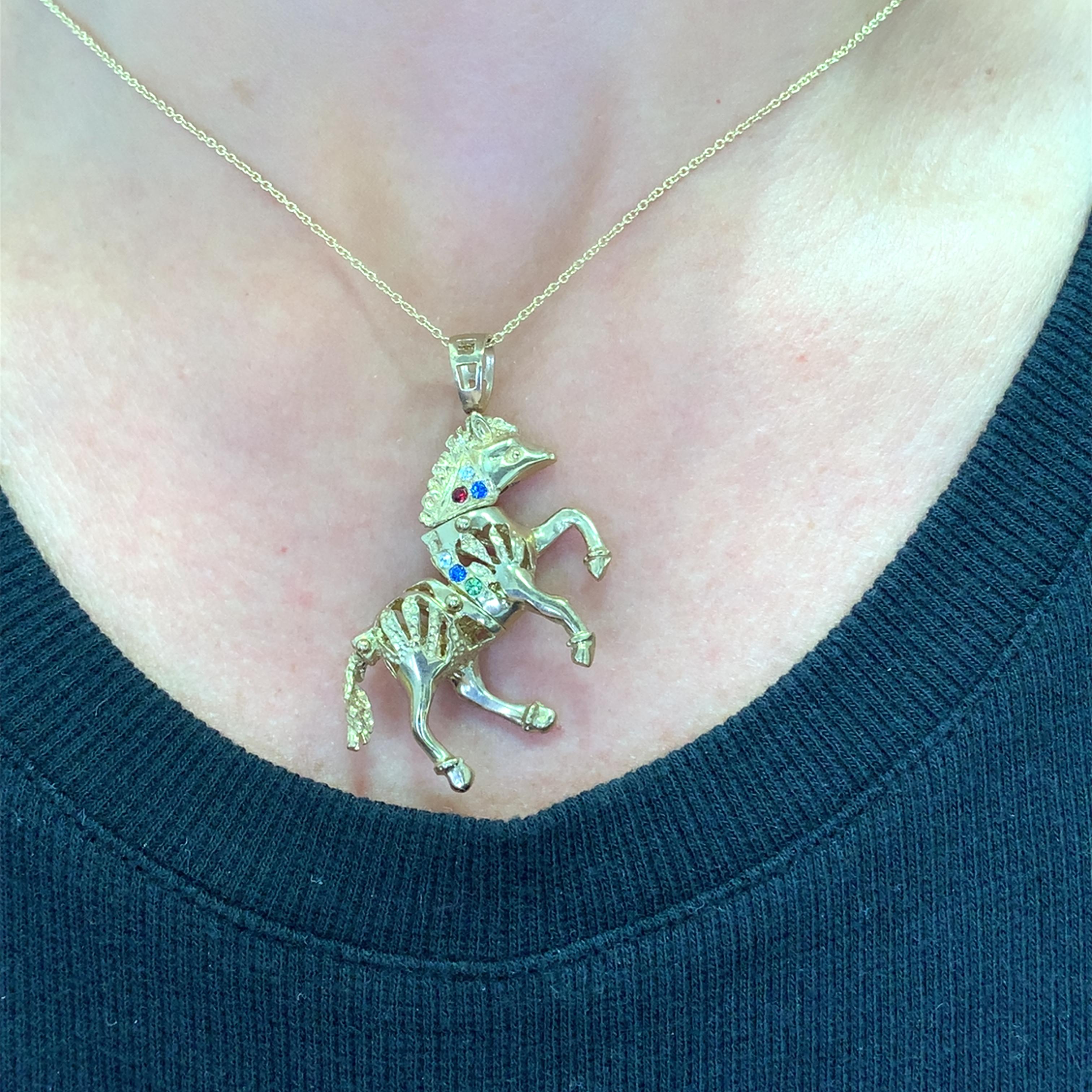 Erhöhen Sie Ihren Stil mit dieser fesselnden Halskette mit beweglichem Pferde-Charme aus Gelbgold. Im Mittelpunkt steht ein sich bewegendes Pferd, das mit seinen runden Edelsteinen, einem Saphir und einem Rubin, in einem leuchtenden Rotton