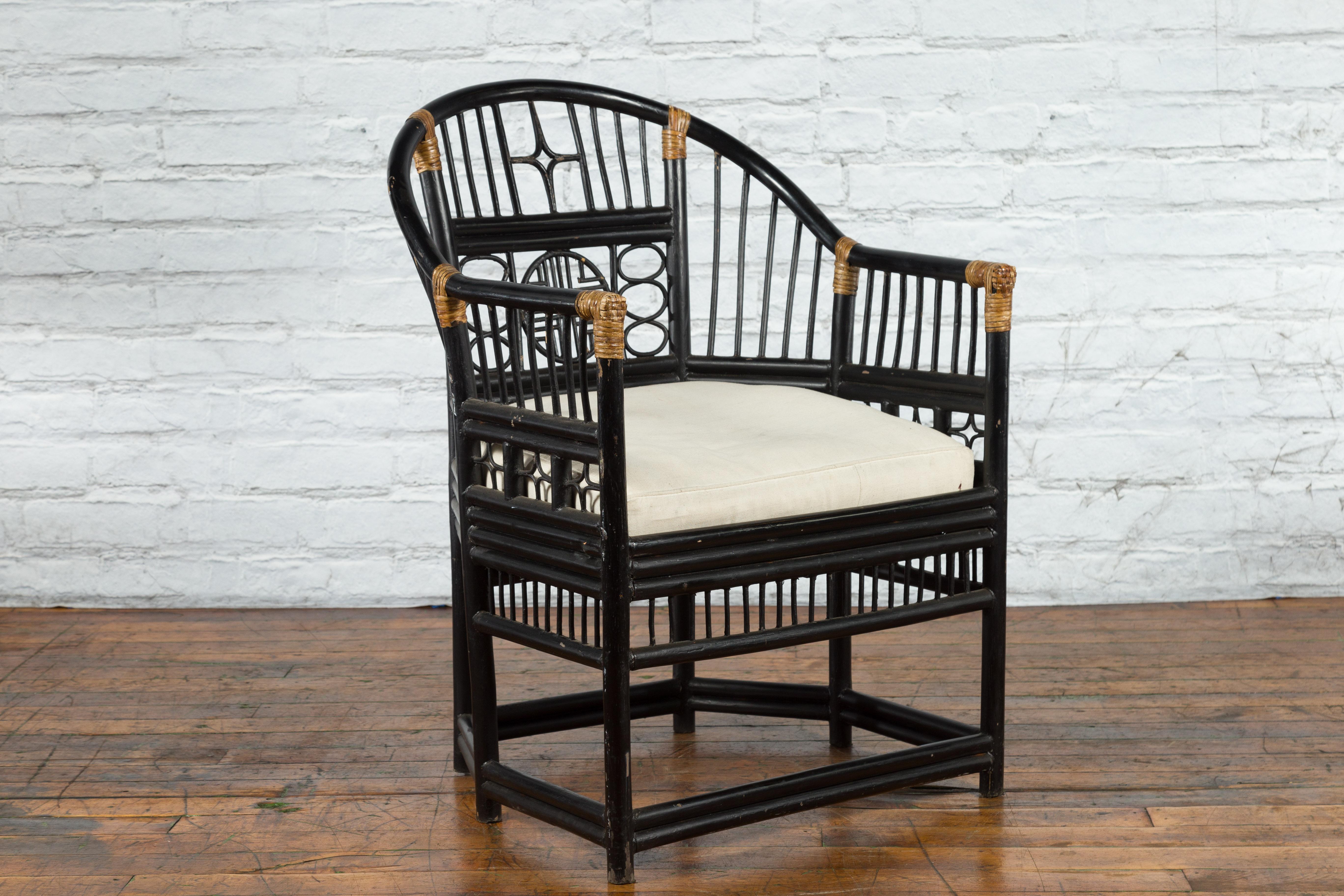 A  horseshoe back black lacquered wooden armchair from the 20th century with bamboo geometric fretwork and cushion. Created during the 20th century, this armchair features an elegant horseshoe back accented in the center with a stylized radiating