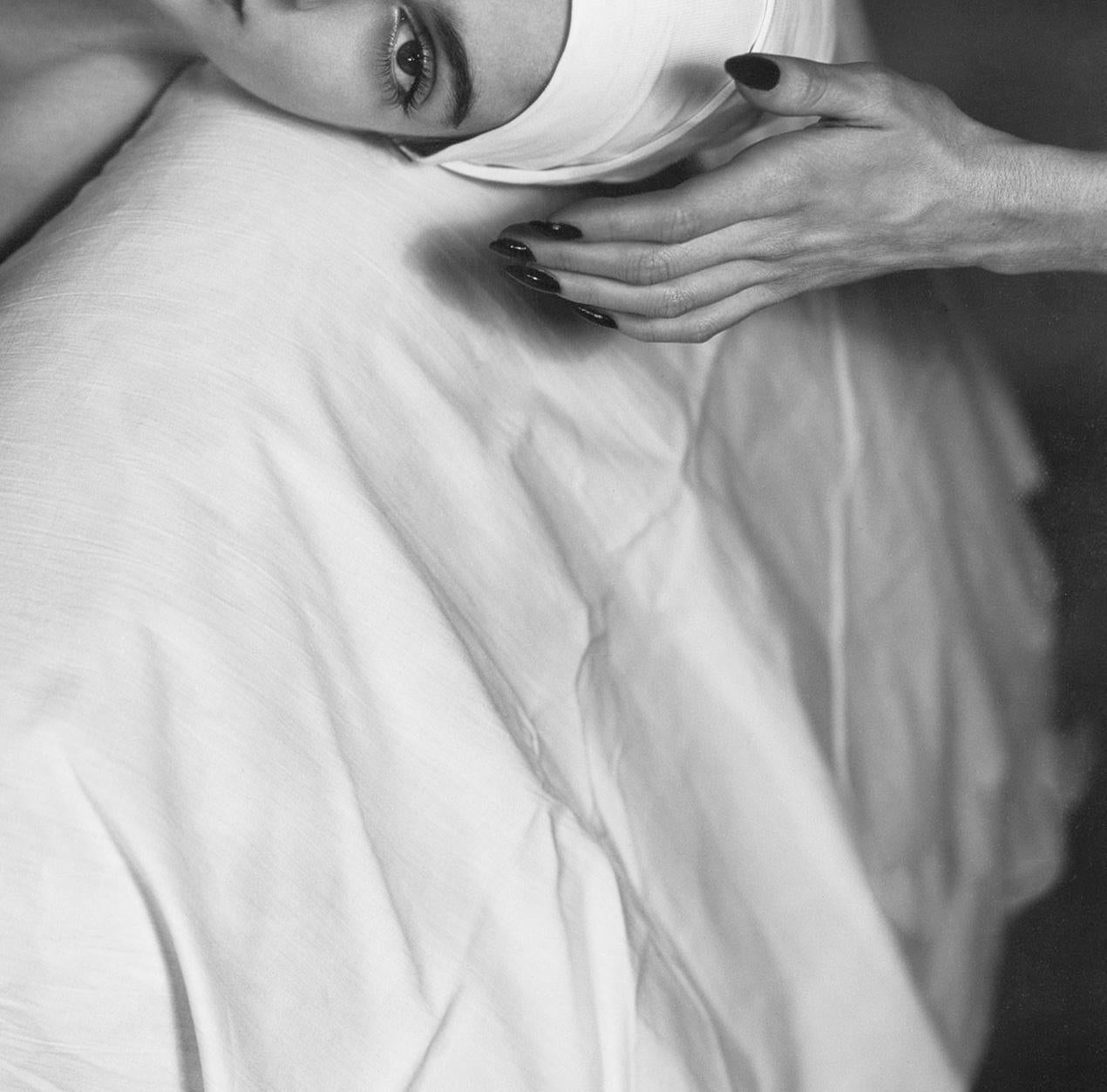This striking black-and-white photograph captures Carmen in NY enveloped in a flowing, white gown, creating a graceful, sculptural form. Her head is elegantly tilted to the side, framed by her delicate hands which convey a sense of introspective