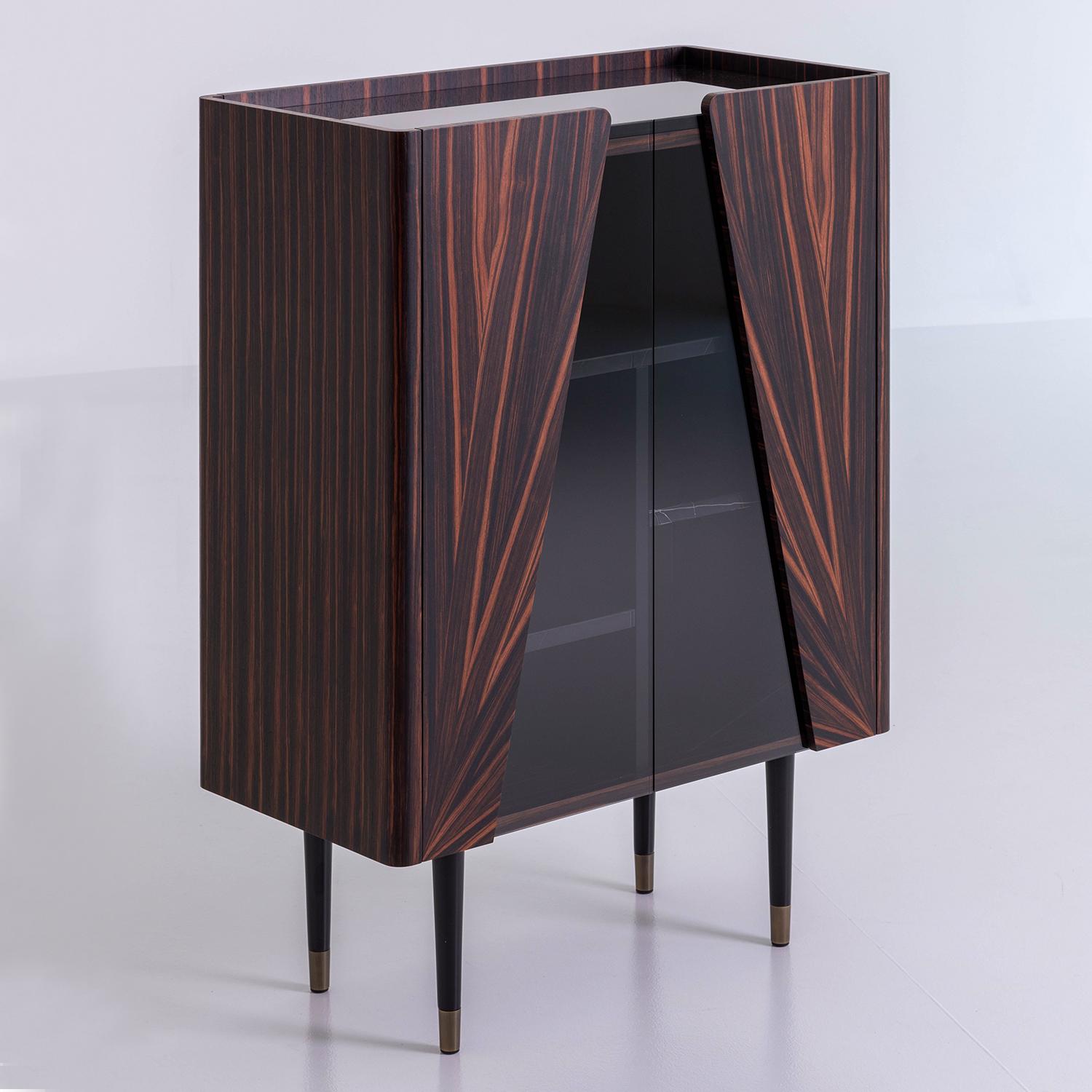 Bar Cabinet Hortz with structure in Ebony wood
With 2 doors made of smocked glass and ebony 
Wood. Including 3 shelves in emperador marble, 
Inside in black lacquered finish with led lighting system.
With 4 black finish legs with solid brass