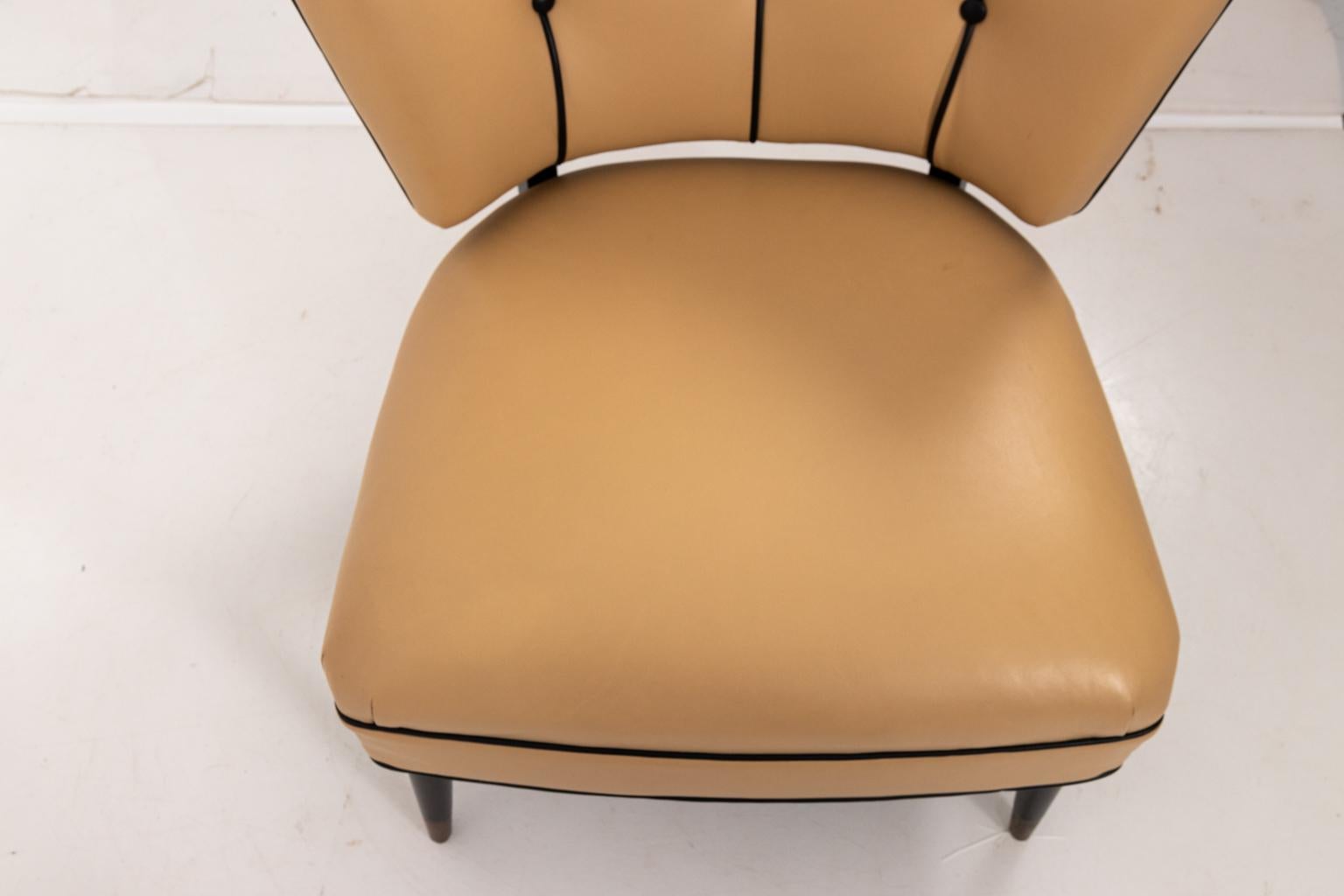 Hostess side chair in the manner of Williams Haines, circa mid-20th century. The piece features Chamois color leather upholstery, black leather piping trim, and tufted buttons on the seat back. The legs are in ebonized wood with brass caps. Please