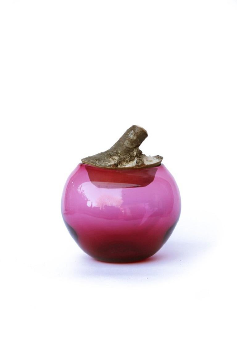 Hot Pink Branch Bowl, Pia Wüstenberg.
Dimensions: D 16-18 x H 20.
Materials: glass, wood.
Available in other colors.

A playful jar, with a lid made from a branch stub following the curvature of the glass. Branch Bowls are blown without a