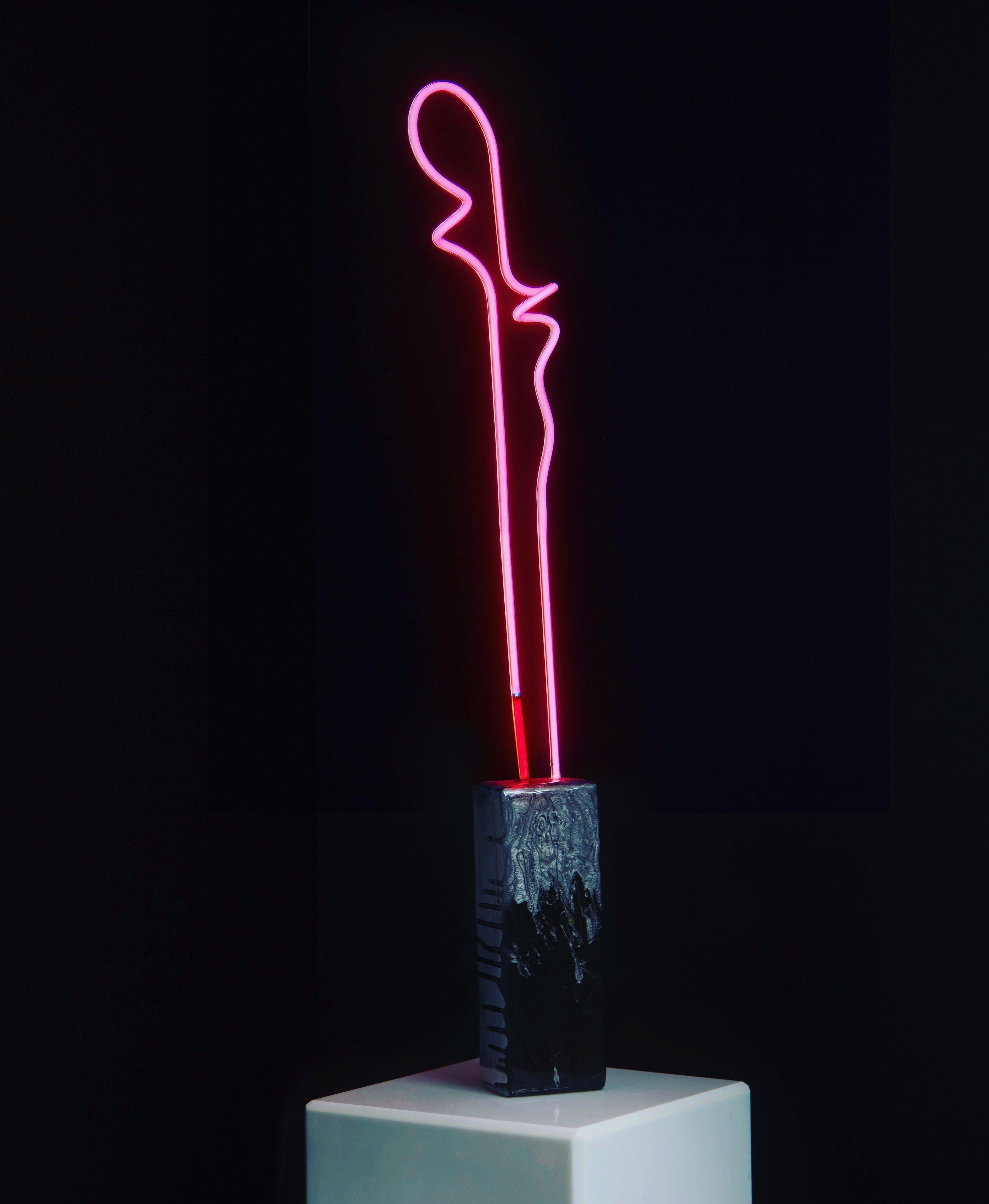 This glass neon table lamp is hand bent neon glass from Italy. One of a kind light sculpture in hot pink with 4” of ruby red- set with pigmented resin in an aluminium base. Transformer is attached so it simply plugs in. All my neon light sculptures