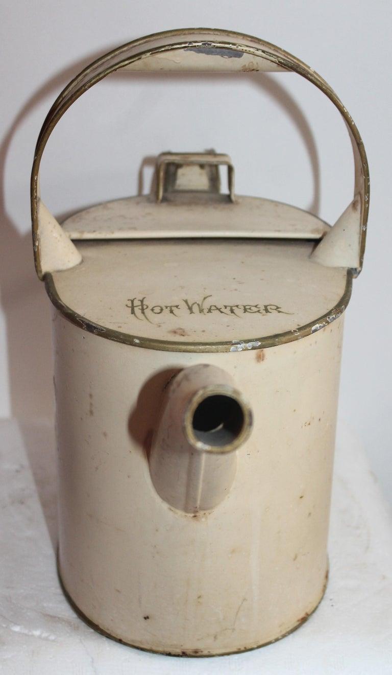 19th century hot water canister in original cream or oyster painted surface. The top of the canister it reads “HOT WATER” in original gilded letters. The can has a newer painted black bottom coat of paint. This was probably done to protect its base.