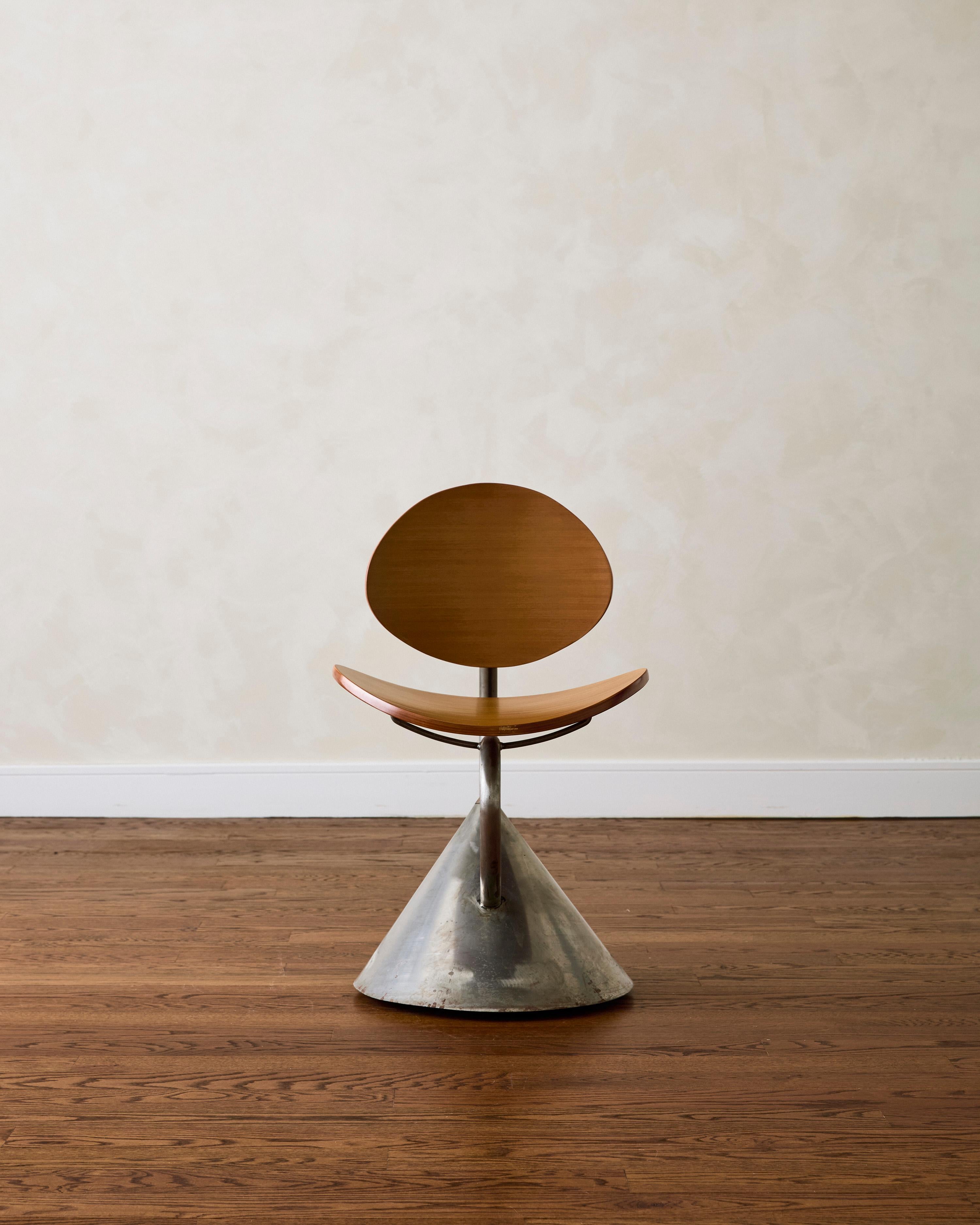 The 'Hotel Zeus' chair, designed by Ron Arad in 1992 and produced by Zeus—the design collective founded in 1984 by Maurizio Peregalli—features a bent ash plywood seat and backrest supported by tubular steel. The steel supports extend from a conical