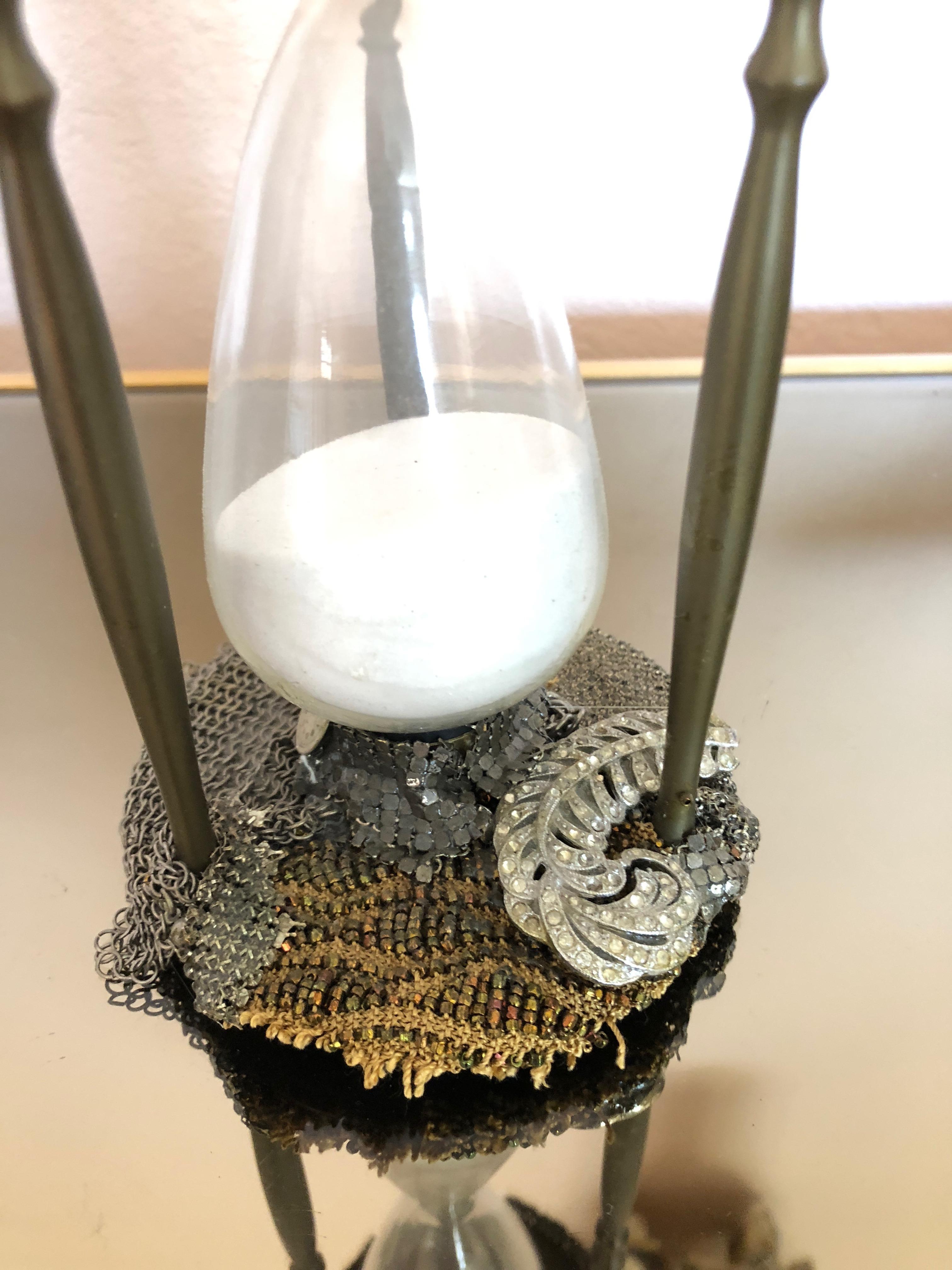 Imaginative sculpture titled The Moment having a vintage found object hourglass encrusted with bits and pieces from mesh silver and gold handbags, watch faces, ceramic skull and hot water faucet. Charming and thought provoking. Signed on bottom, Fay