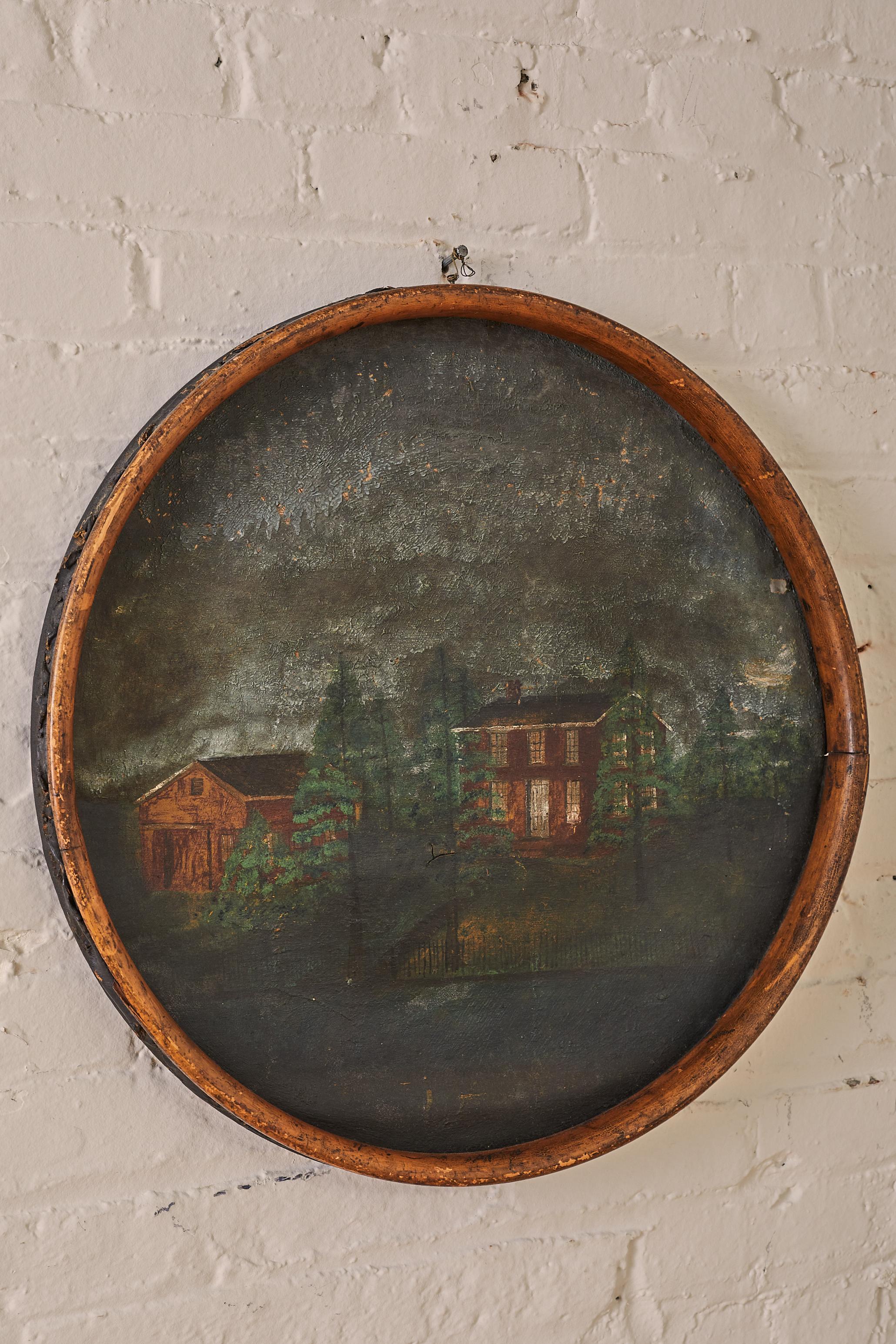House Landscape on Oil Cloth. This artwork depicts a house, garage, fence, all nestled amidst trees. The canvas is stretched over a wooden bicycle rim.

