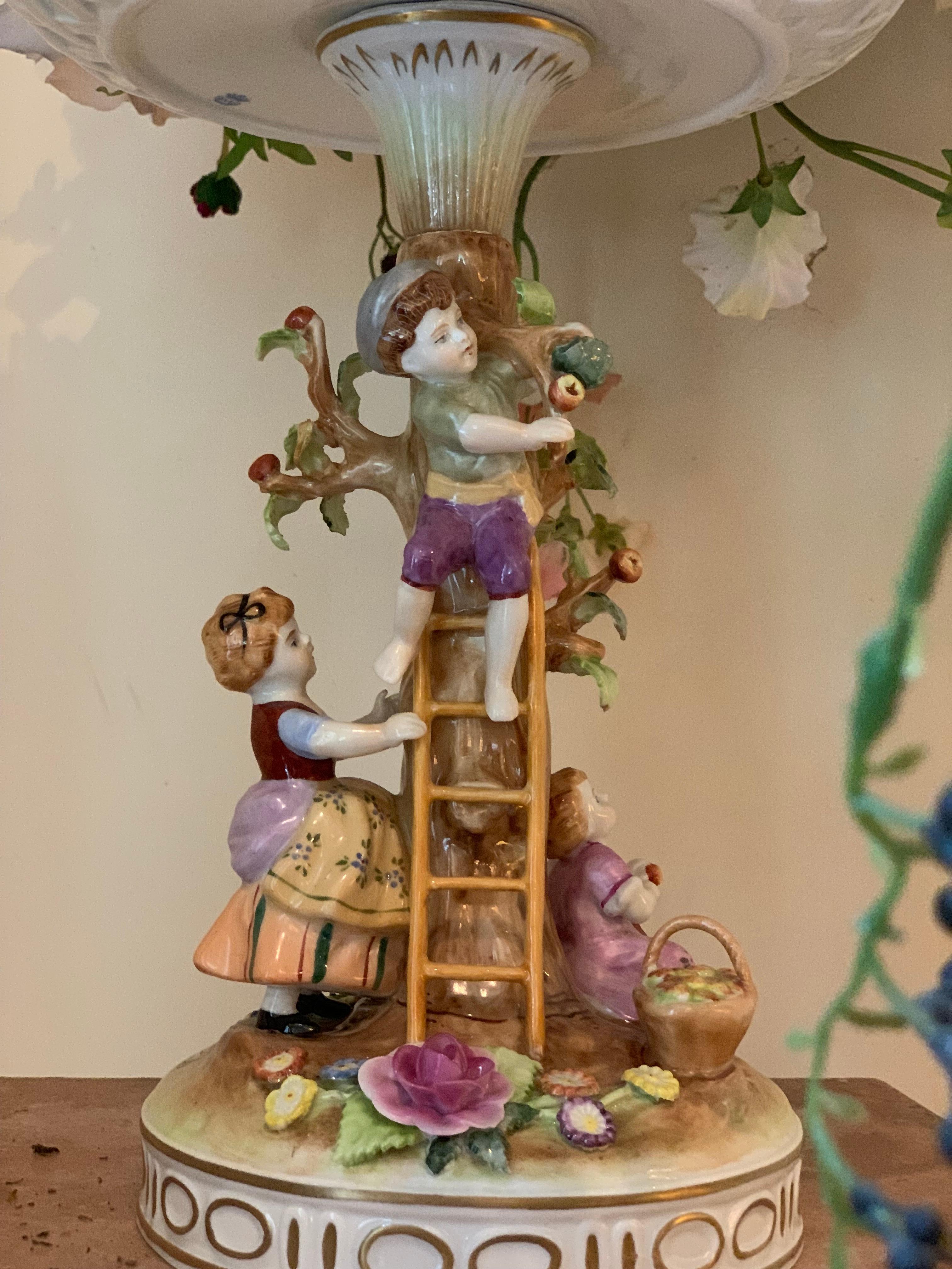 House of Schierholz Plaue is founded in 1890. This porcelain flower box is manufactured in Germany, before 1989. The object are figures, children at an apple tree. Above is a box that can hold flowers. Everything is painted and modulated by hand.