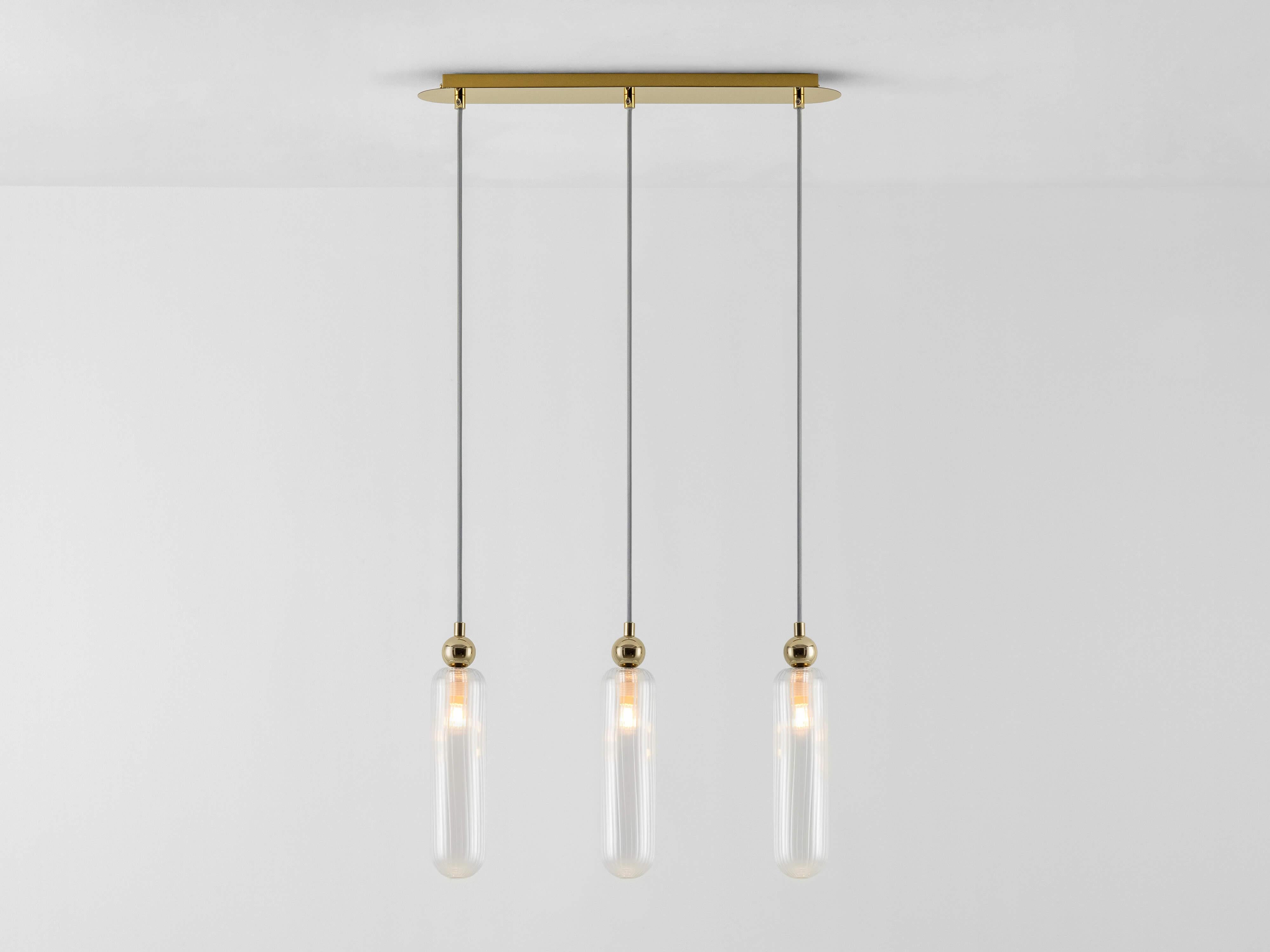 Simple, classic and elegant, this trio of pendants is a beautiful sculptural ceiling light, perfect for your dining, kitchen or living space. Hanging suspended on light grey fabric wires, the ribbed glass shades are complemented by the metalic brass